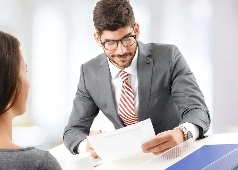 A man in a suit reviews a document while sitting across from a woman