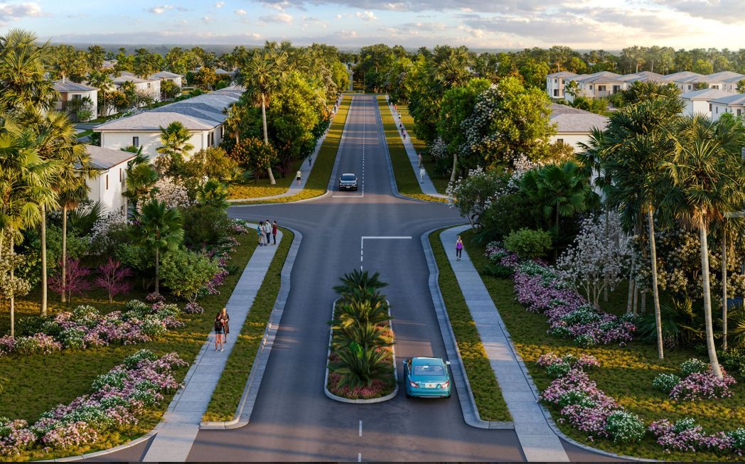 Tree-lined suburban street with landscaped medians, pink flowers, and two cars under a cloudy sky