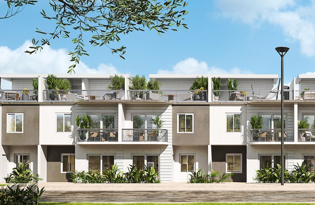 Modern beige apartment building with balconies, greenery, and a streetlamp under a blue sky