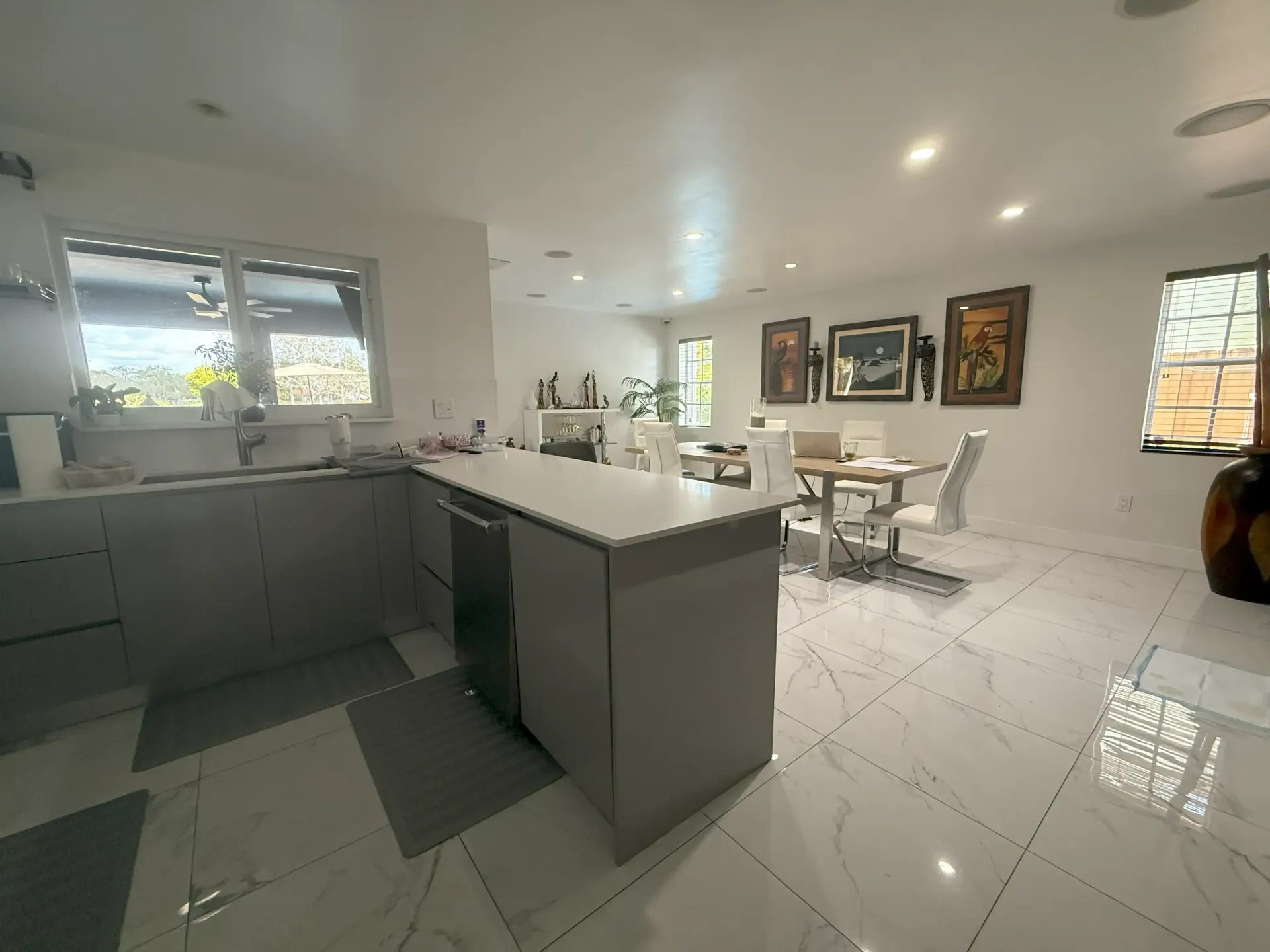 Bright modern kitchen and dining area with gray cabinets, white island, and tiled floor.