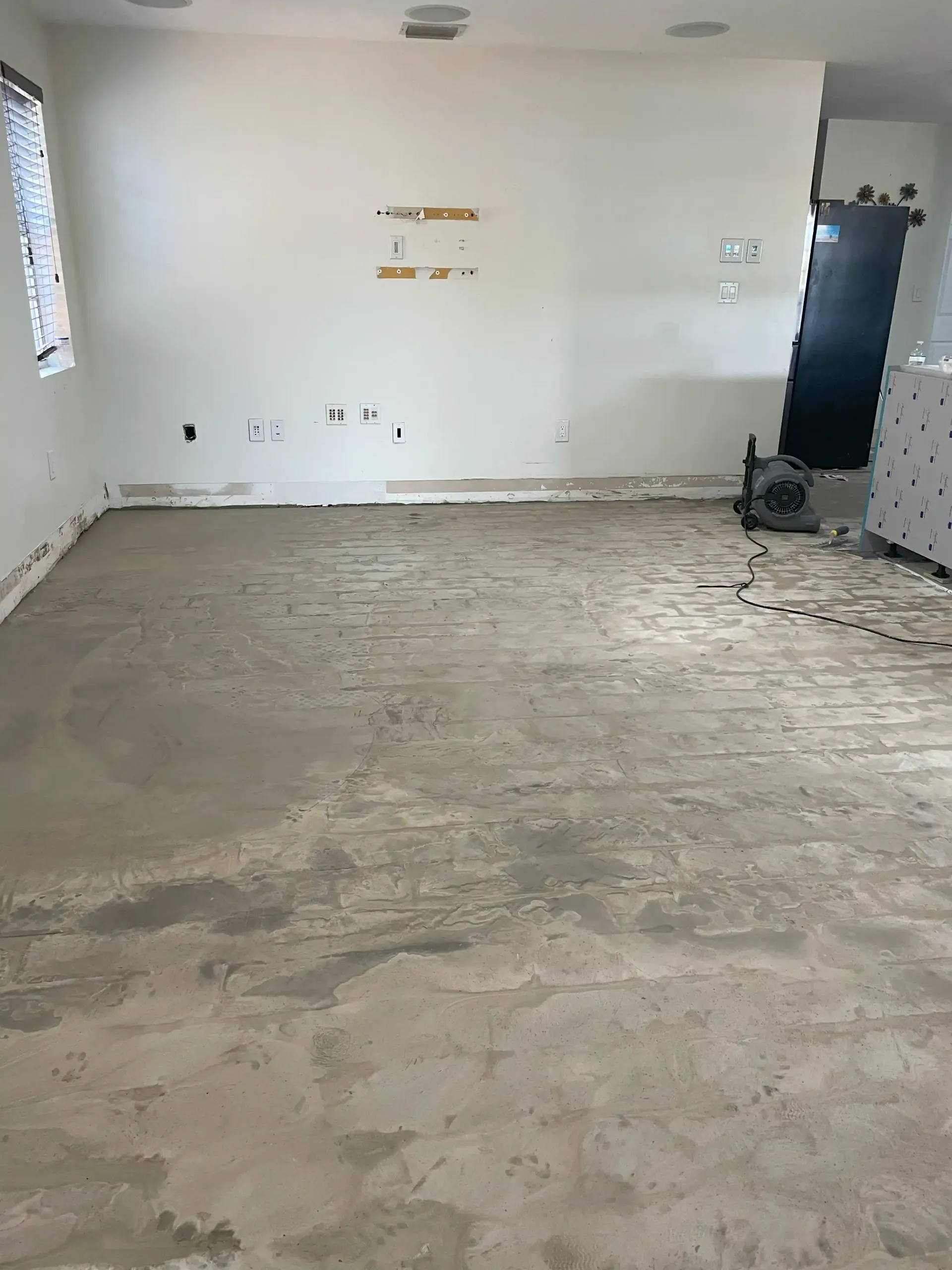 Empty room with unfinished concrete floor, white walls, and a black cabinet near the right wall.