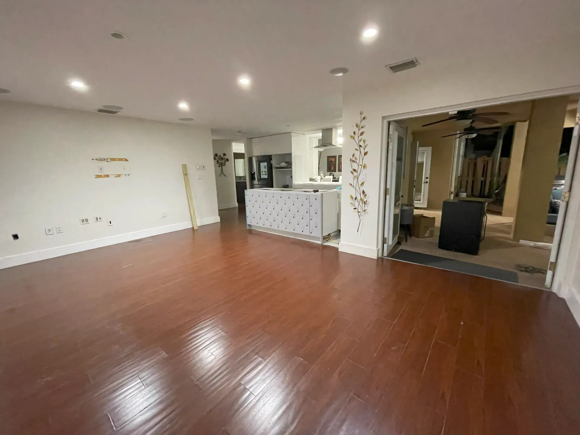 Empty modern room with glossy wood floor, recessed lights, and a small kitchen counter.