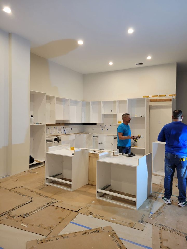 Kitchen under renovation with white cabinets, two workers, and protective floor covering