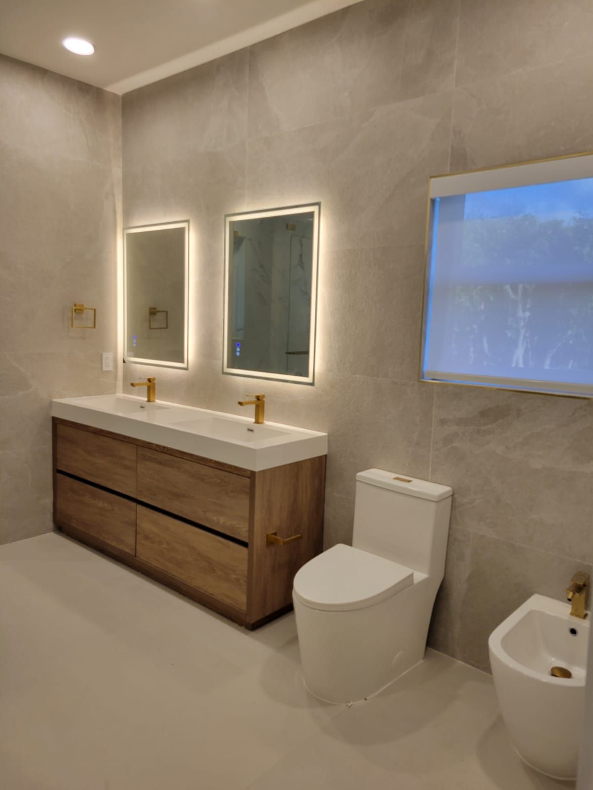 Modern bathroom with wood vanity, double mirrors, toilet, bidet, and frosted window