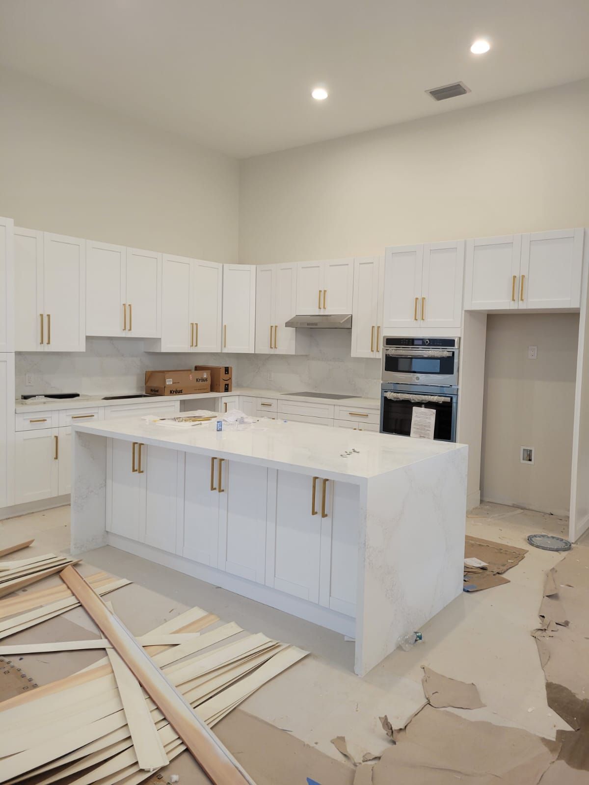 Bright white kitchen under renovation with cabinets, island, marble backsplash, and construction debris on the floor
