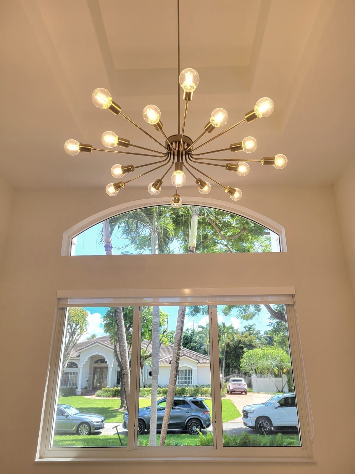 Starburst chandelier in a bright foyer with arched window and view of parked cars outside
