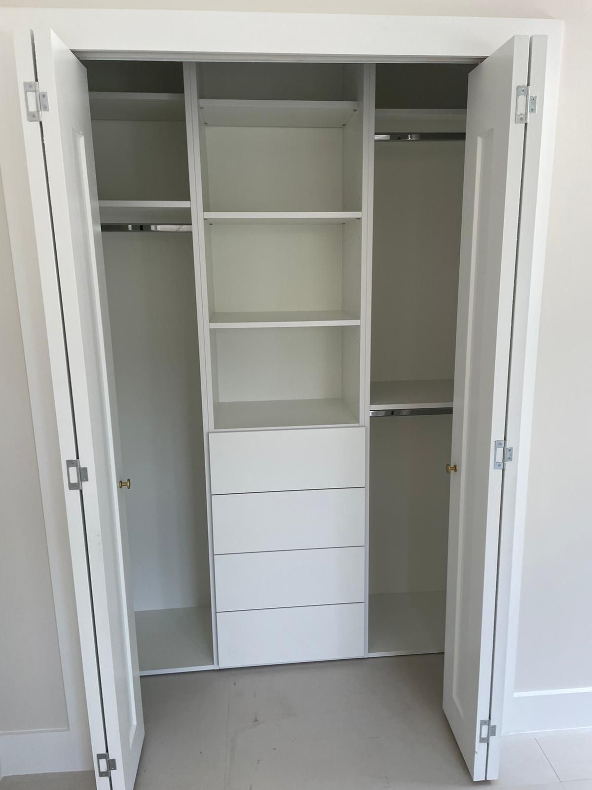 Open white closet with shelves, hanging rods, and drawers in a plain room.