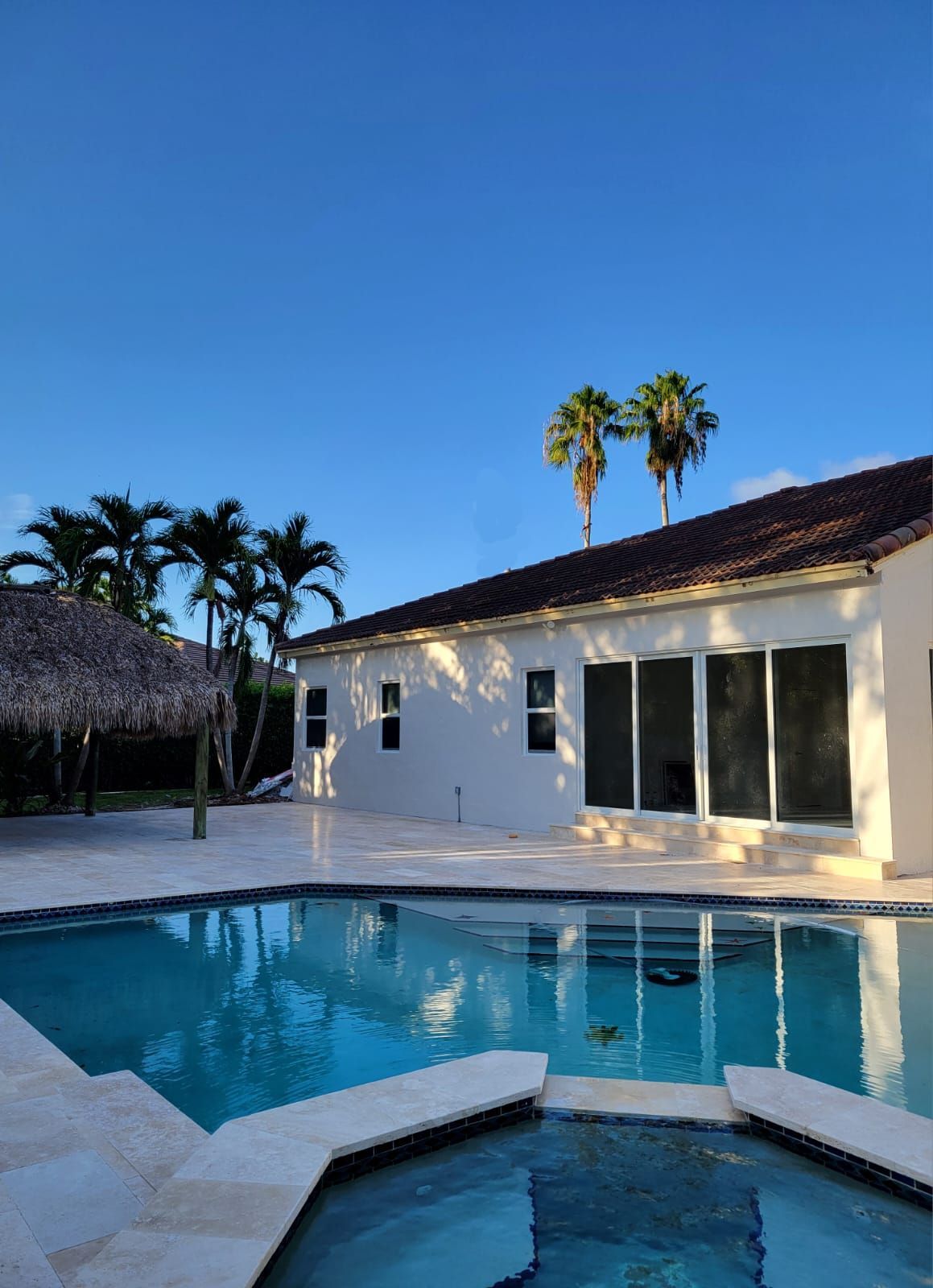 White villa with a turquoise pool and palm trees at sunset under a clear blue sky