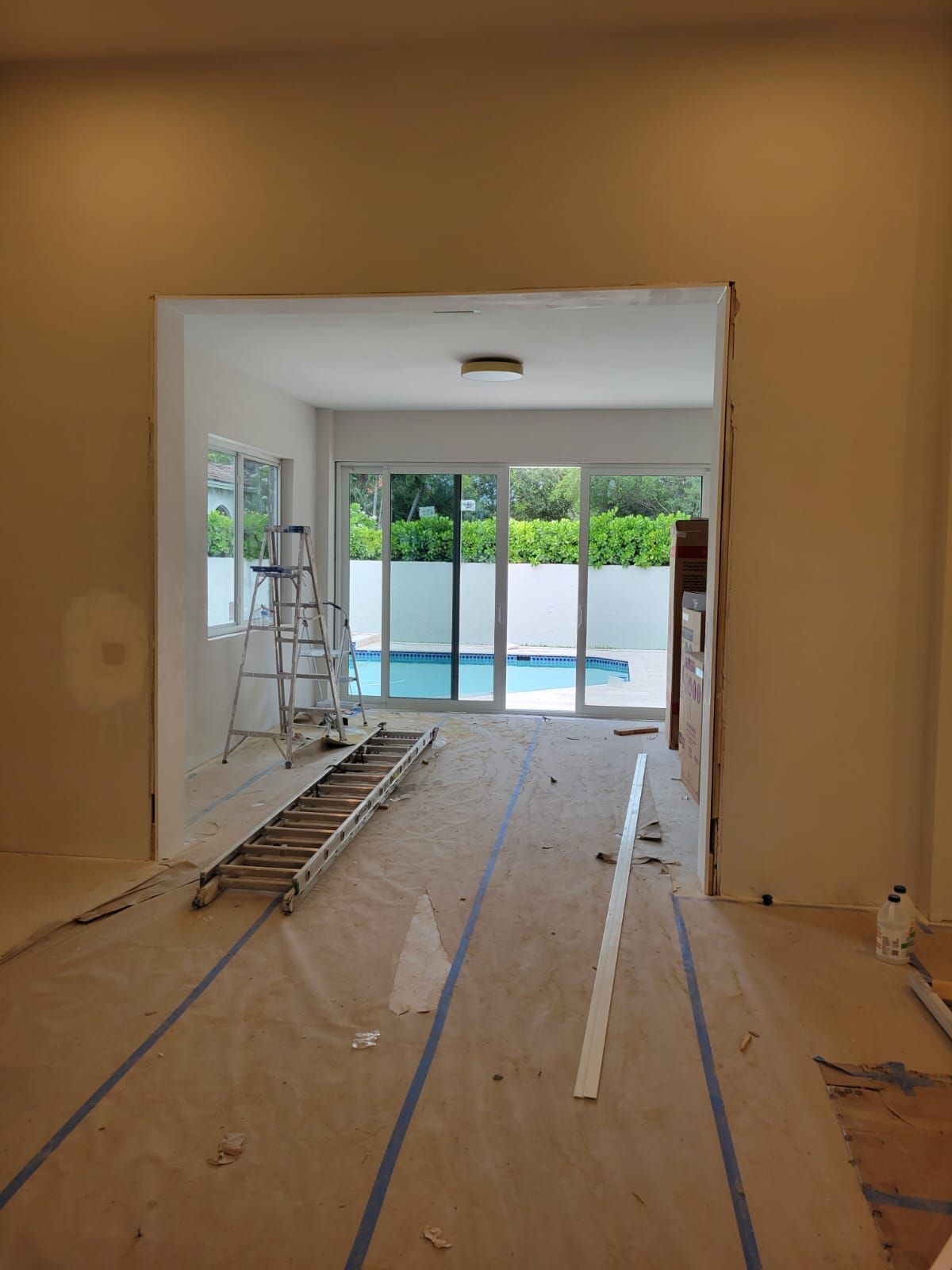 Renovation room with ladder, floor coverings, and sliding glass doors opening to a pool area.