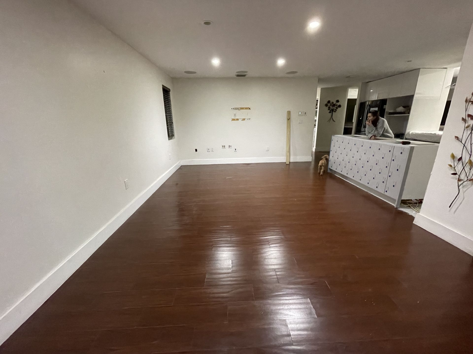 Empty living room with glossy hardwood floors, white walls, and recessed ceiling lights.