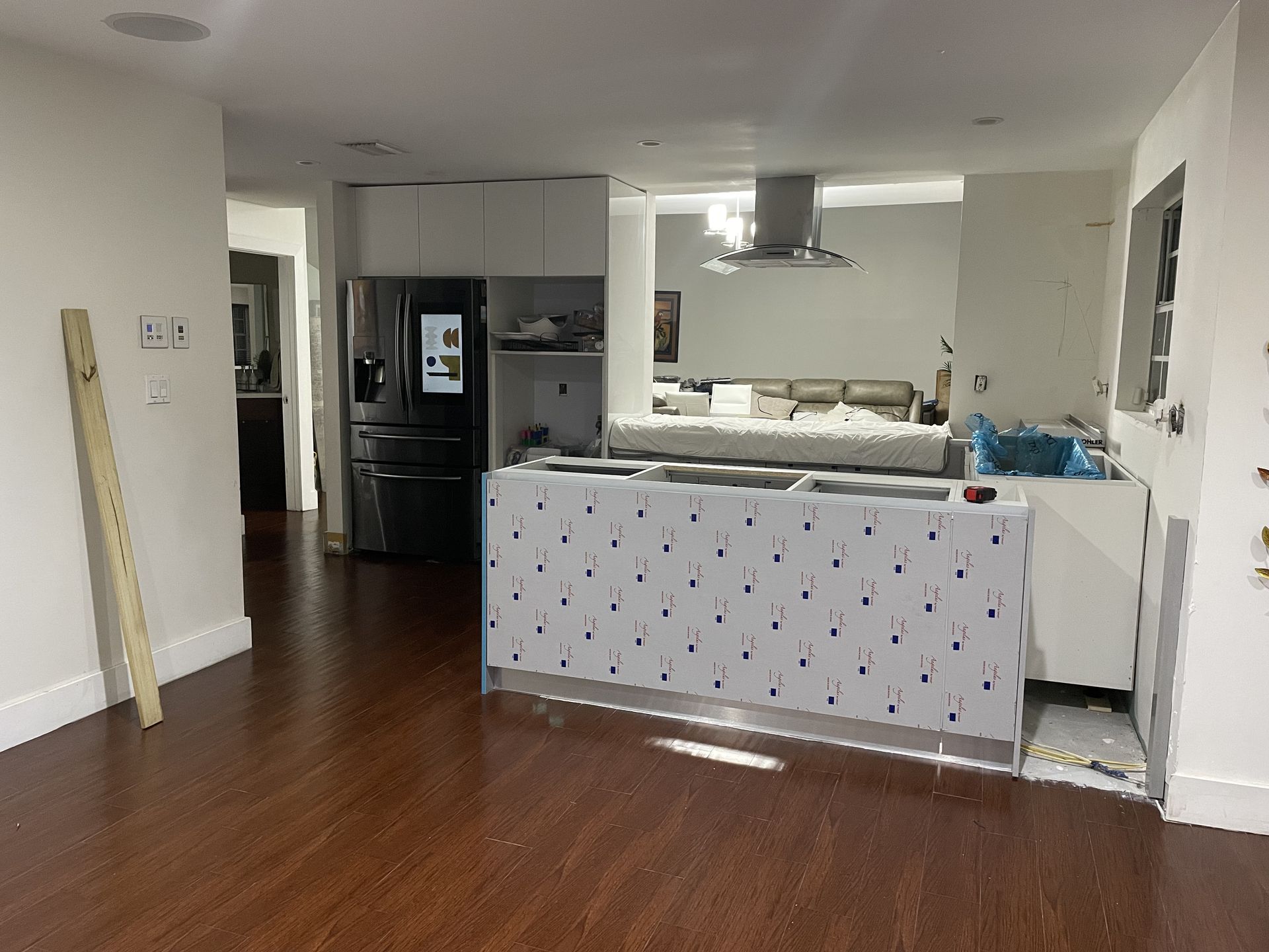 Open-plan kitchen and living area with hardwood floors, white walls, and a patterned island cover.