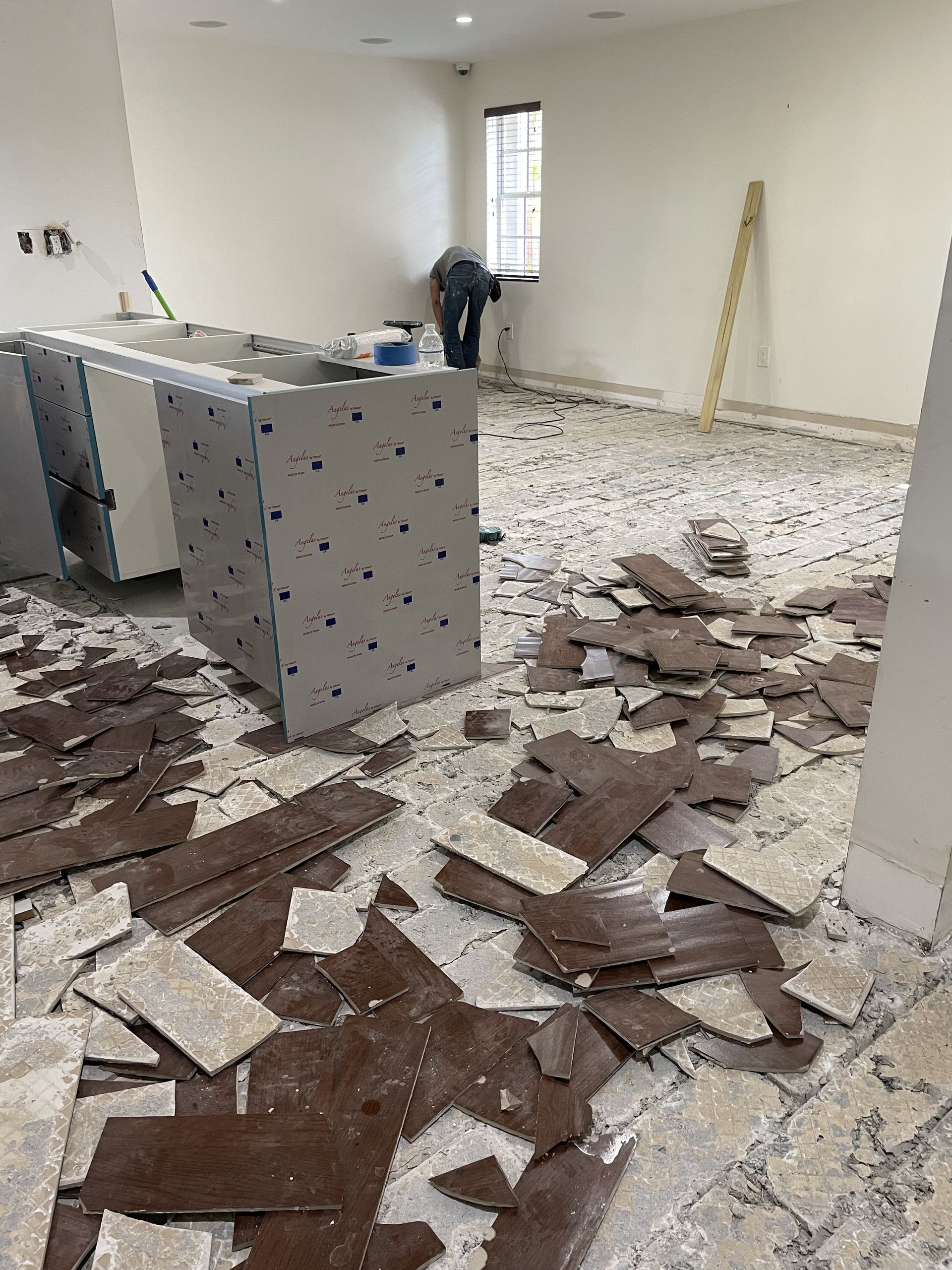 Renovation debris scattered across a room with exposed flooring and cabinets against a white wall