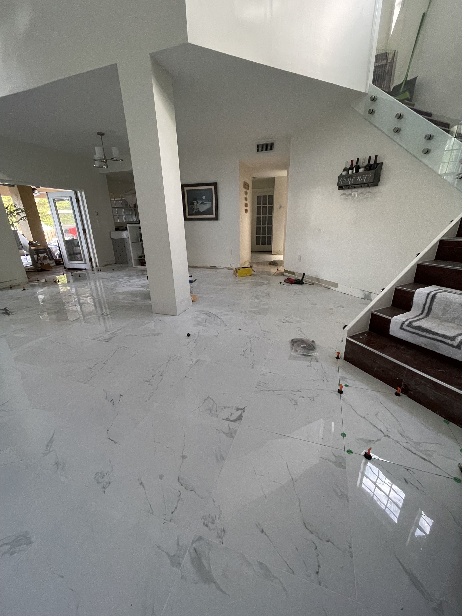 Spacious white living room with glossy tile floor, staircase, and brown sofa in a bright modern home