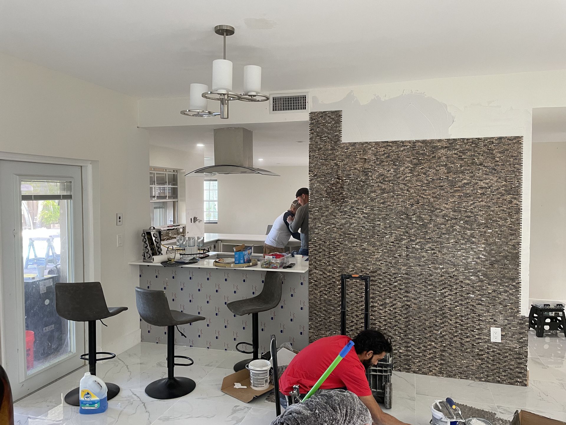 Kitchen under renovation with a worker kneeling by a wall and another person near the island.