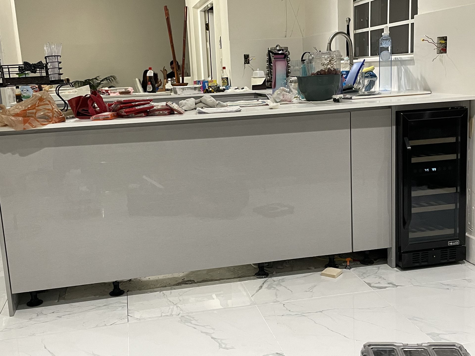 Kitchen counter with scattered items and a small black mini-fridge beside it, in a white room