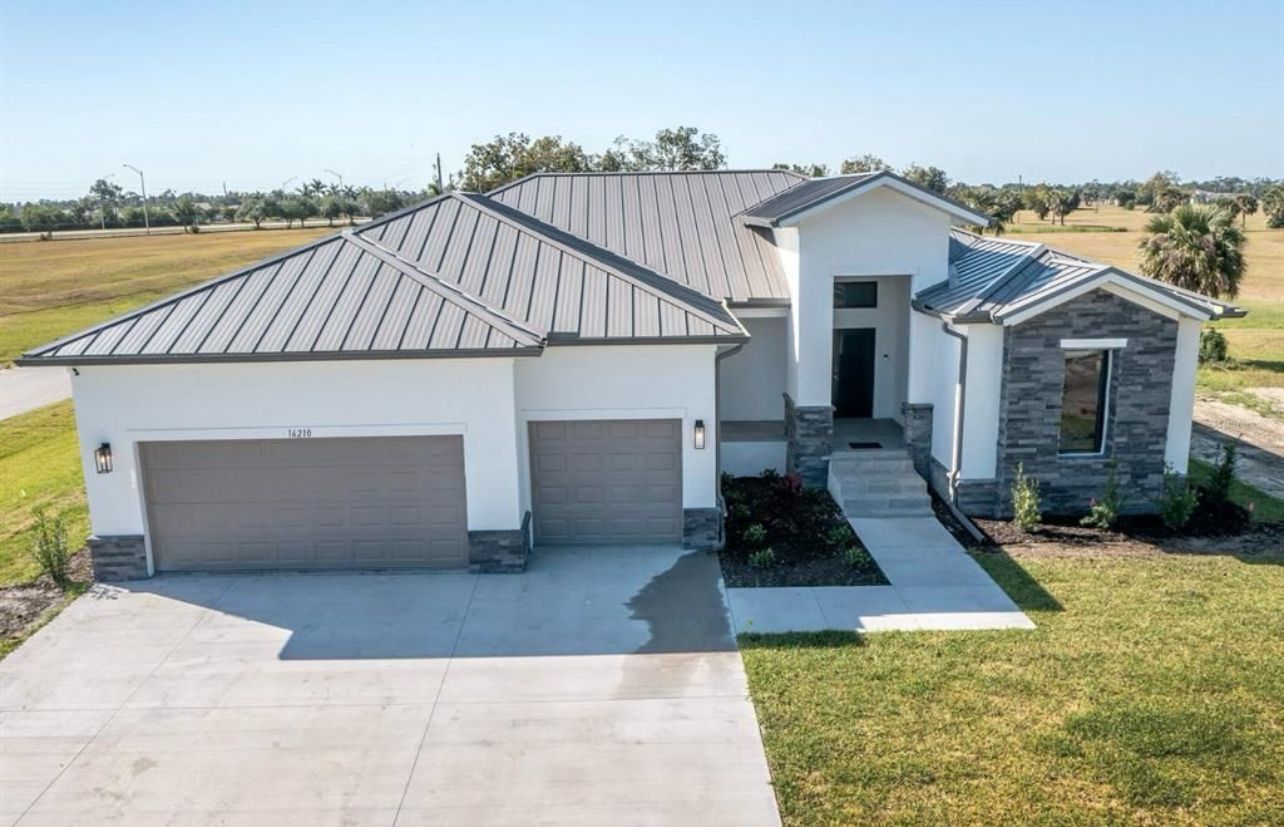 Modern white house with gray metal roof, three-car garage, and front lawn in a rural setting