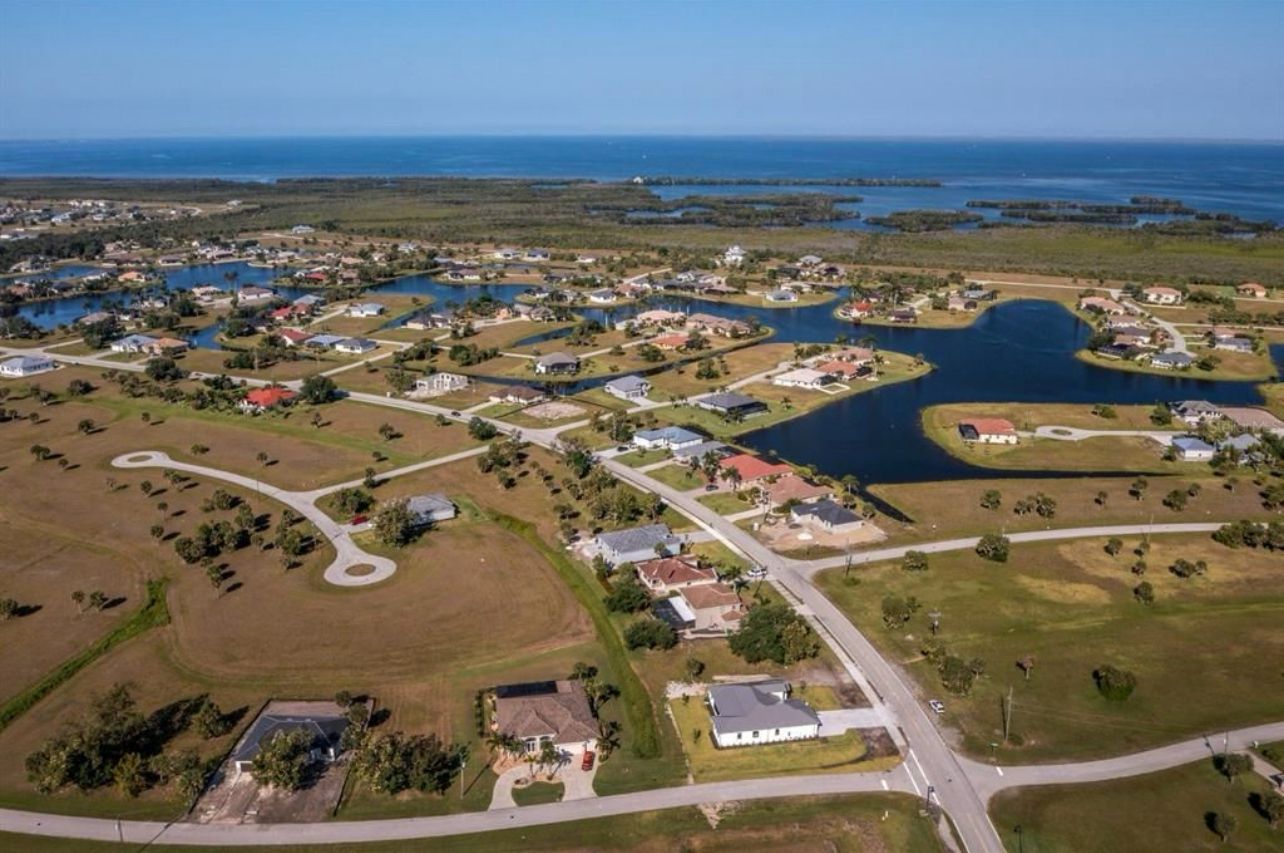 Aerial view of a coastal neighborhood with houses, roads, waterways, and ocean in the distance