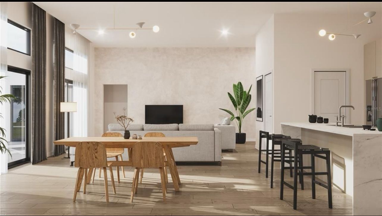 Modern open-plan living room and kitchen with wood dining table, white sofa, bar stools, and large windows.