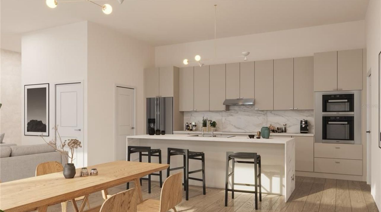 Modern white kitchen and dining area with island, wood table, and built-in ovens