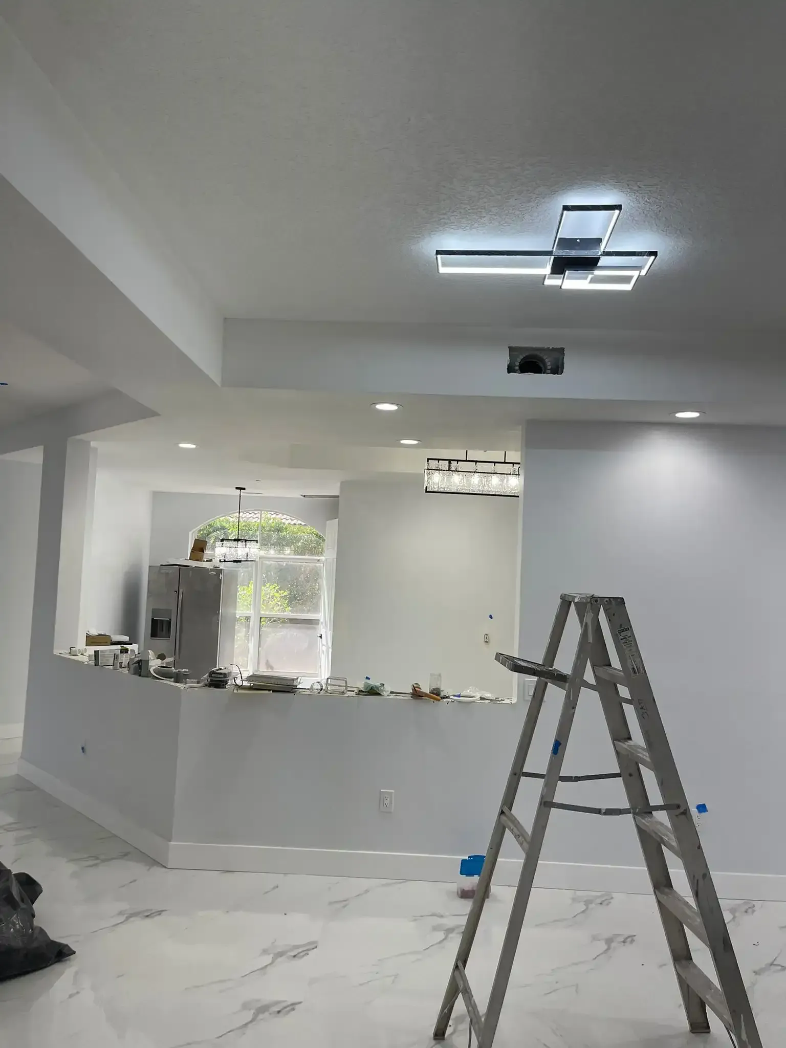 Modern kitchen under renovation with ladder, ceiling light being installed, and debris on the floor