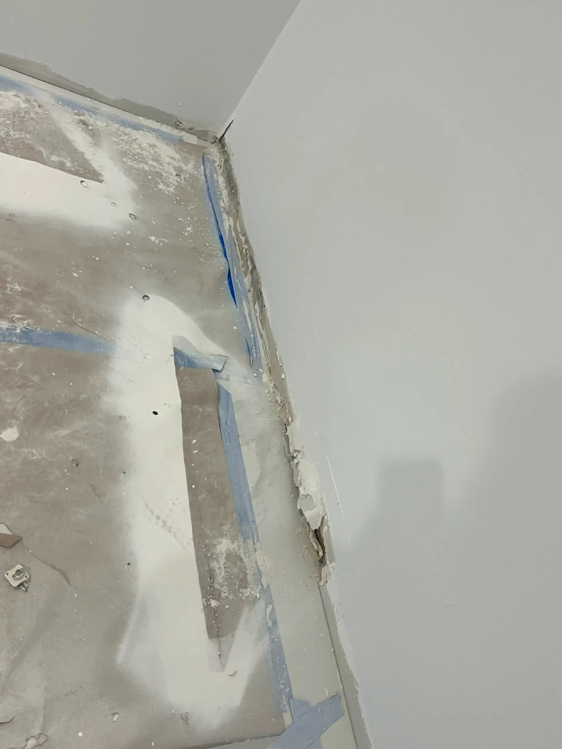 Close-up of a wall corner with blue painter’s tape and white patching compound around a repair area