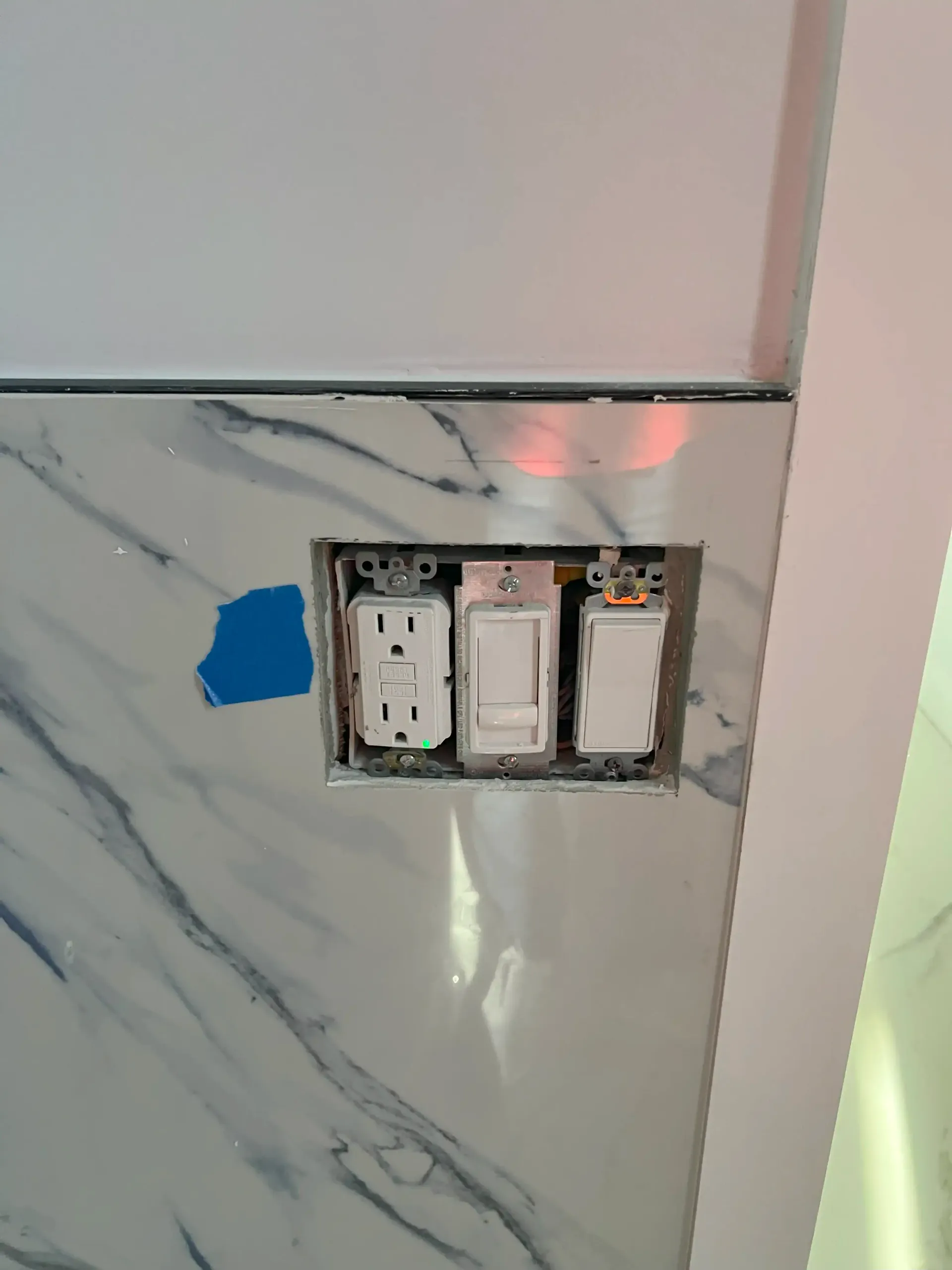 Wall outlet and light switch panel on a marble-patterned wall, with blue painter’s tape nearby.