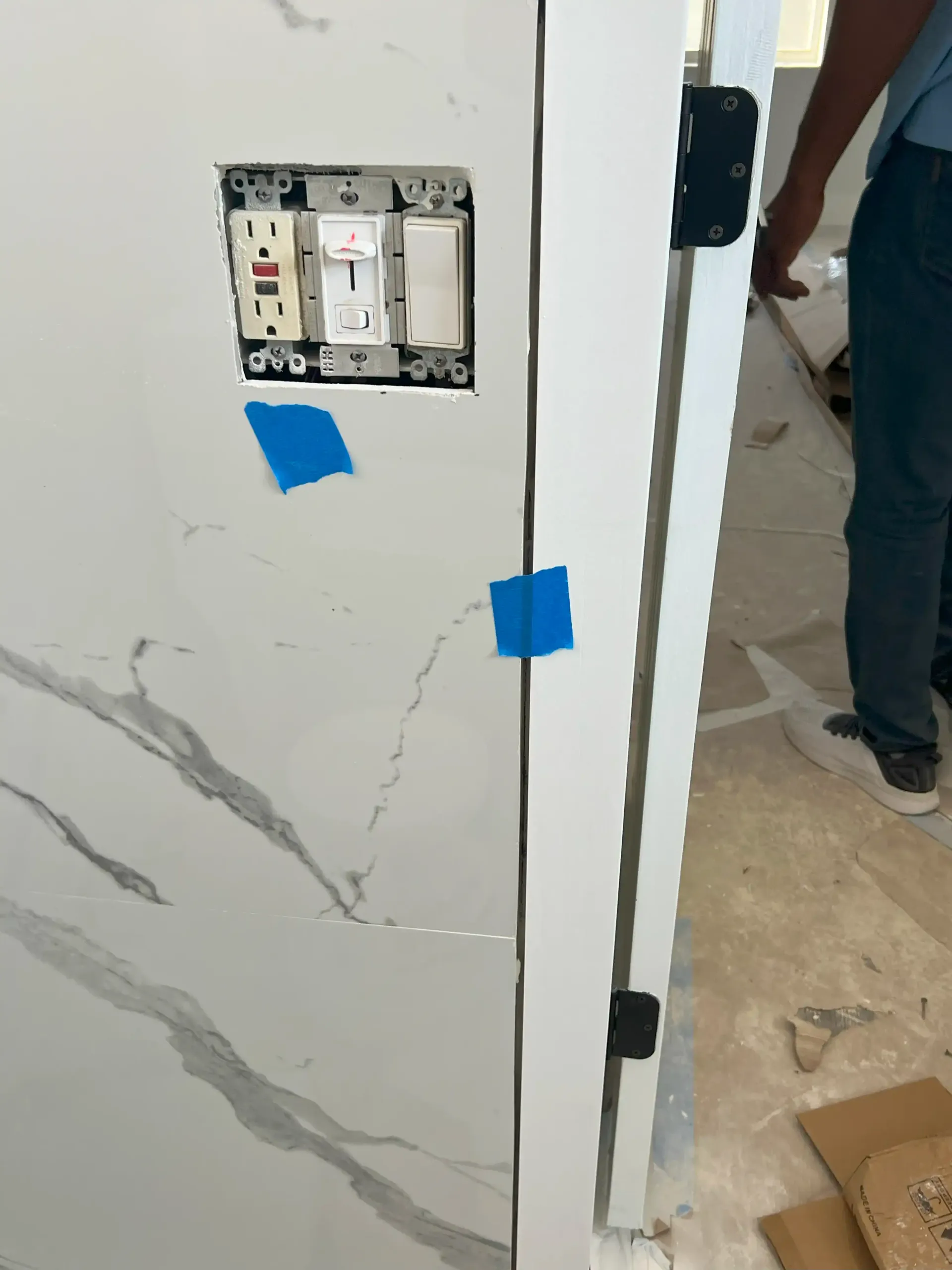 Partially installed wall panel with exposed electrical switches and blue tape in a hallway
