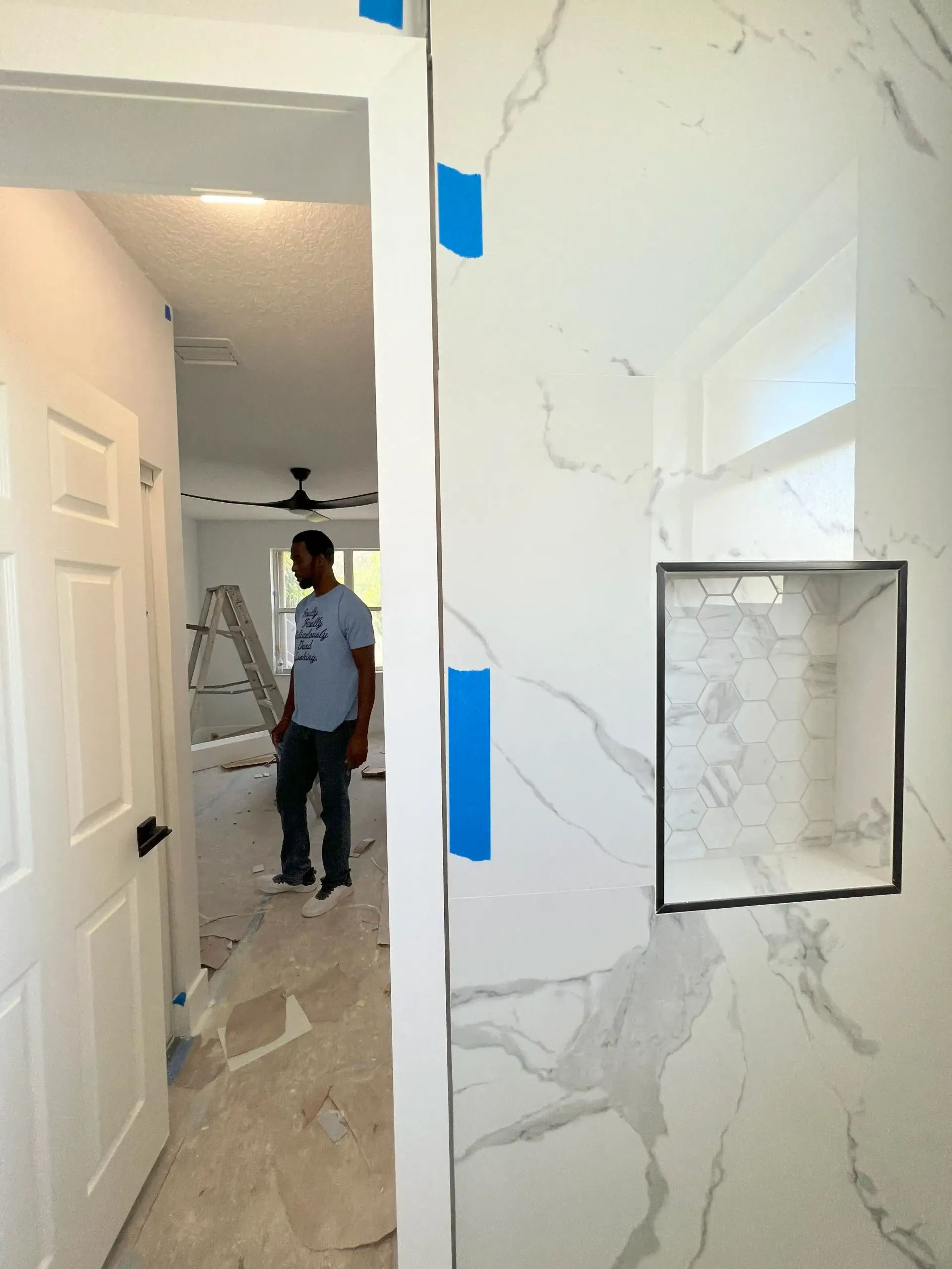 Hallway under renovation with marble-look walls, blue tape, and a worker in the background