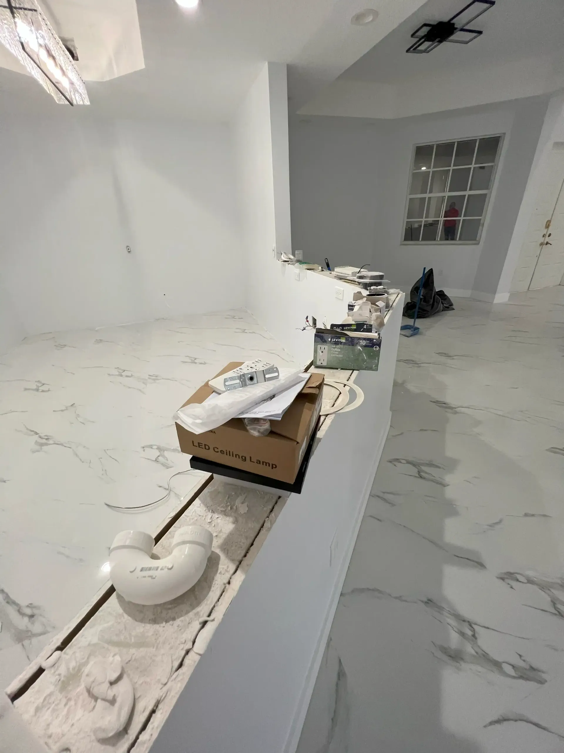 Bright white empty room with marble-look floor, half wall, and scattered paint supplies on the ledge