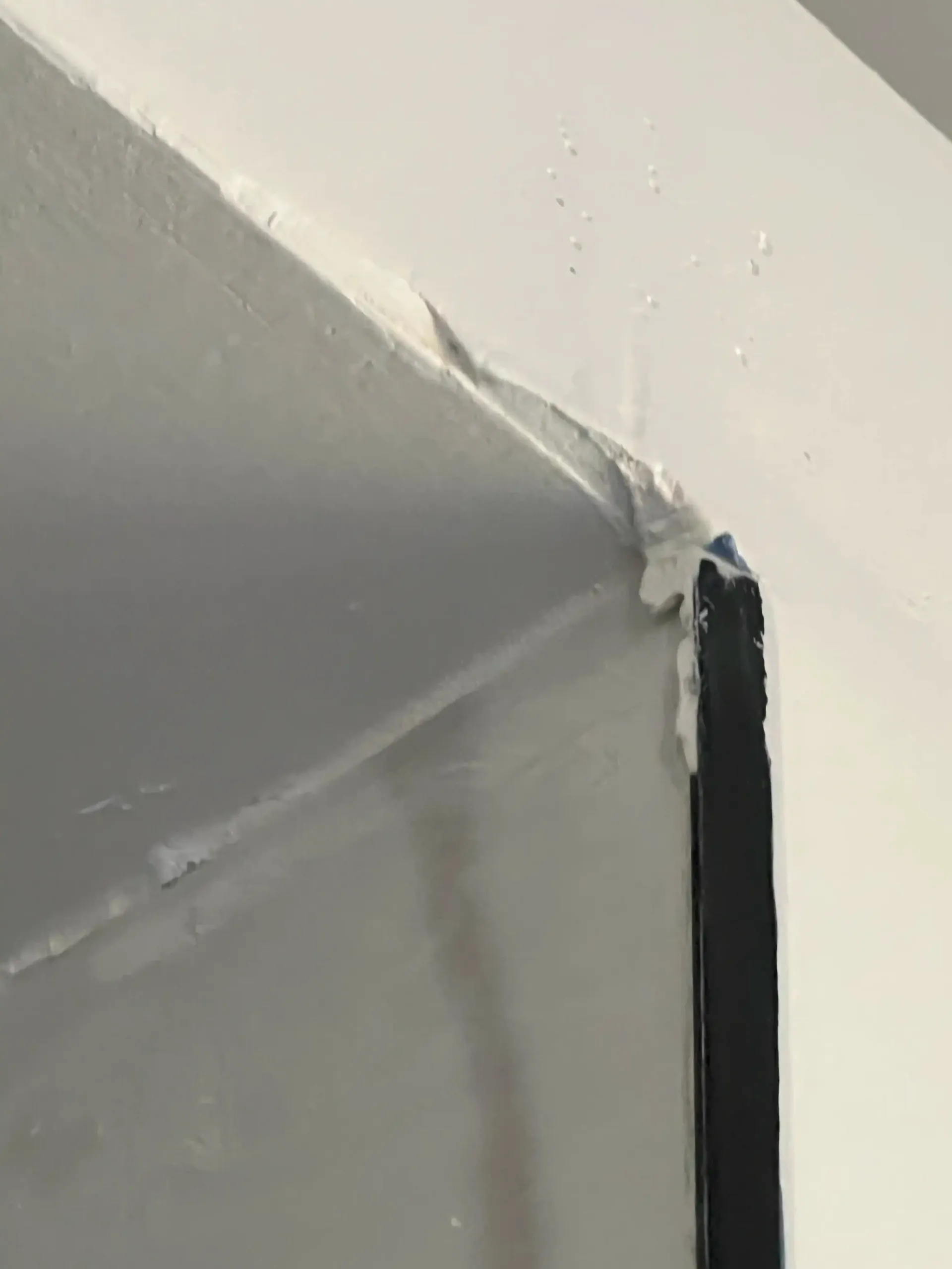 Close-up of a white wall corner with peeling paint and a black vertical trim strip