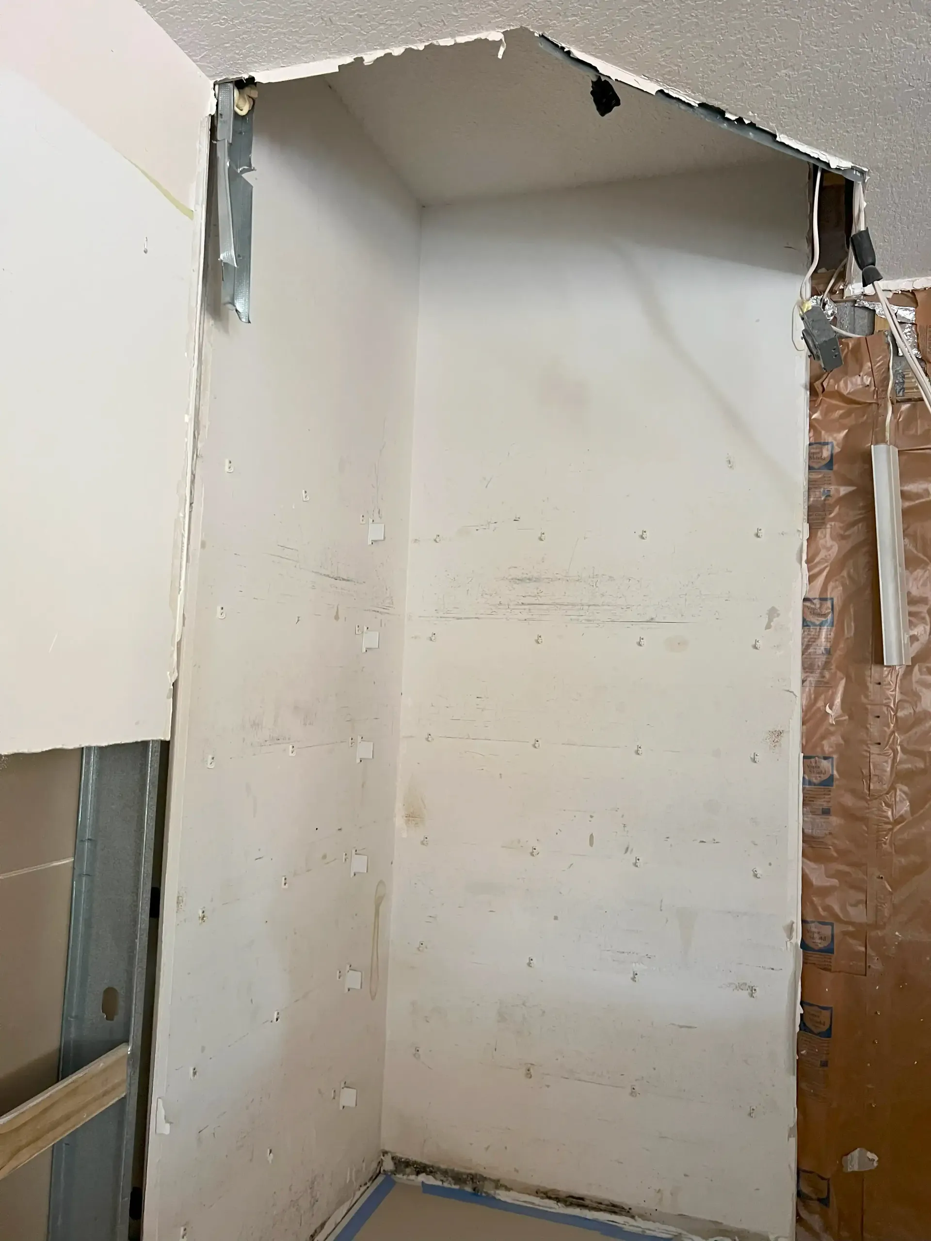 Damaged wall opening in a room, with exposed framing and unfinished drywall edges