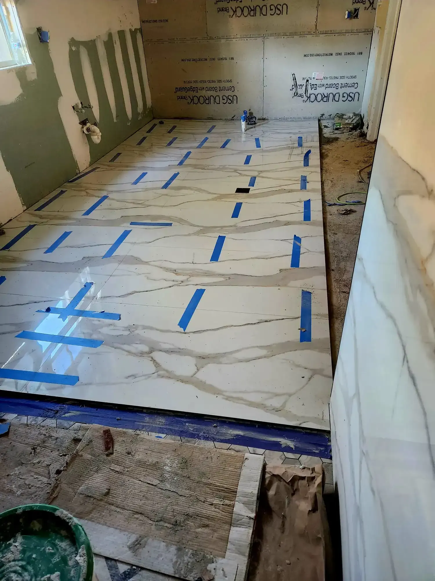 Tape-covered floor in a bare room under renovation, with white protective sheeting and unfinished walls.