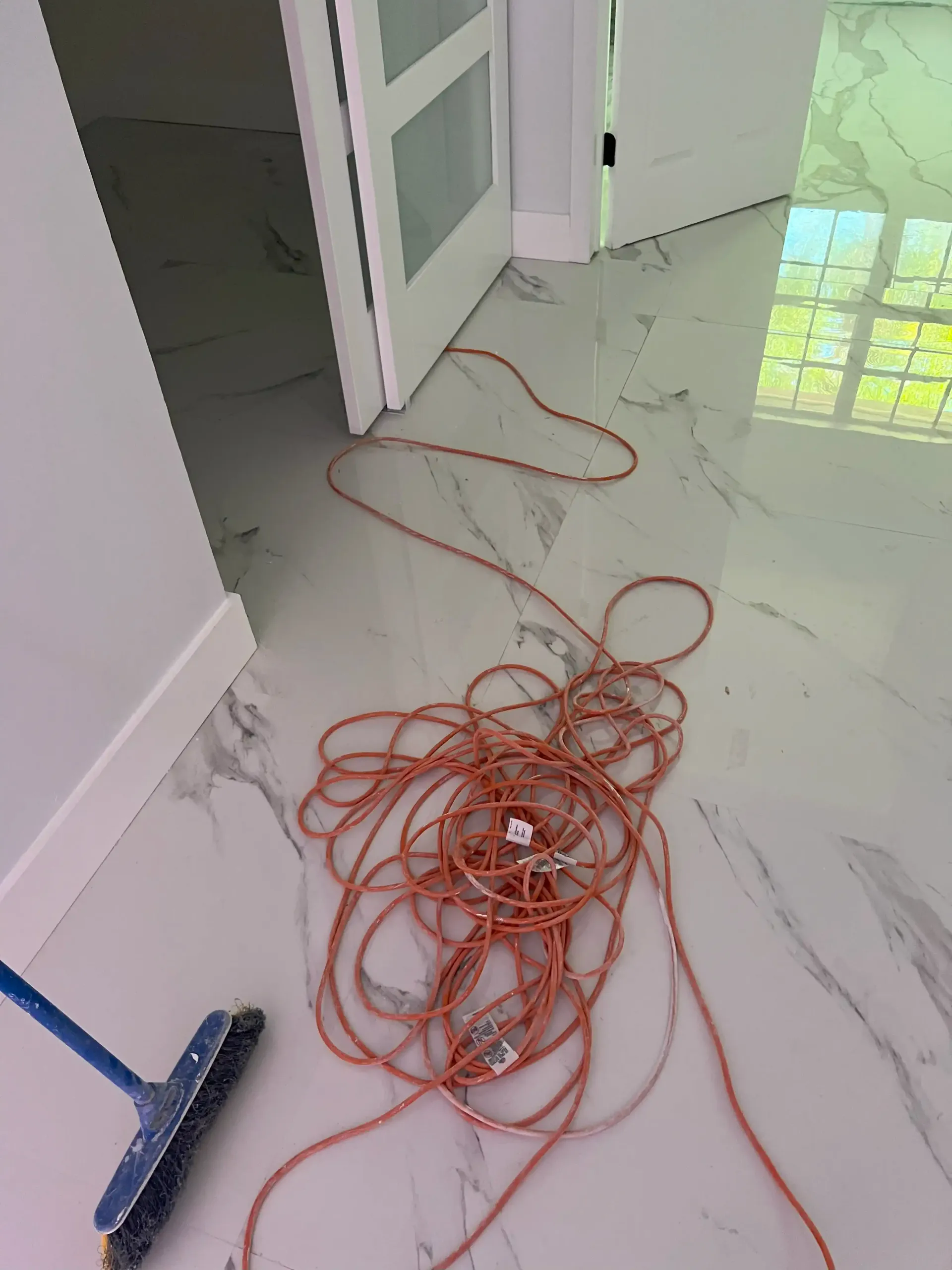 Tangled orange extension cord on a white marble floor beside an open door and broom