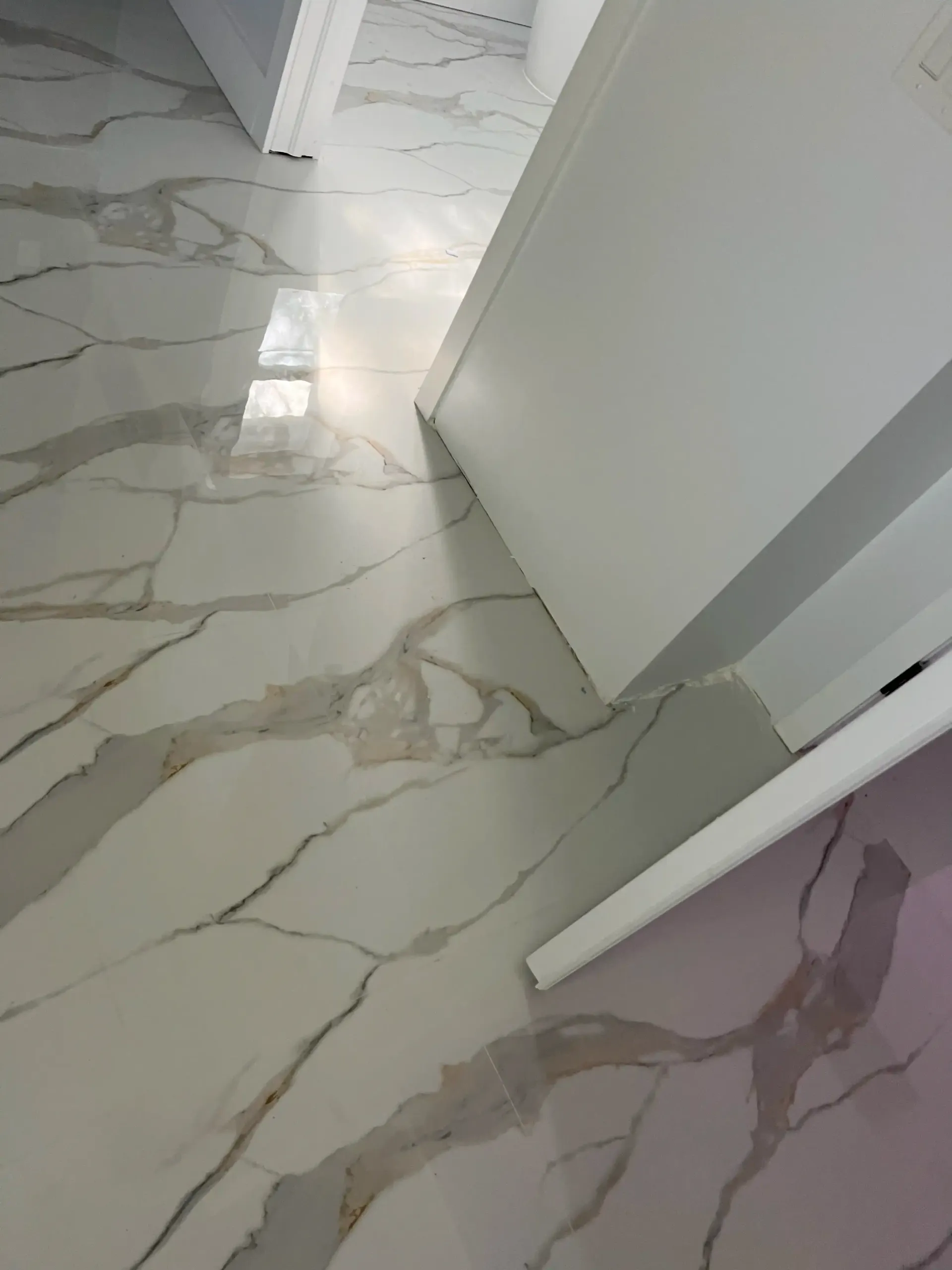 White marble-tile floor in a hallway with open doors and bright sunlight reflections