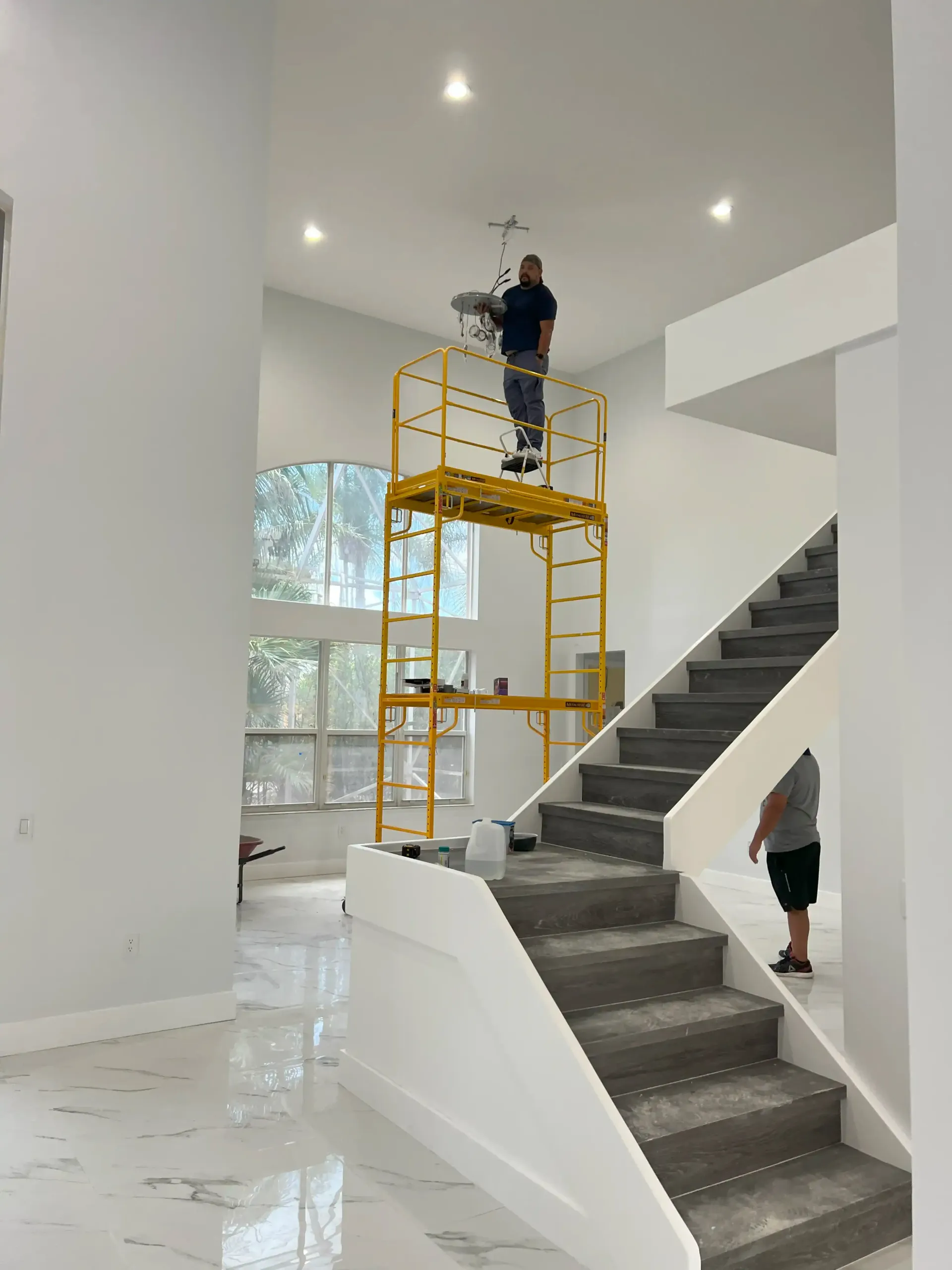 Worker on yellow scaffold painting a high ceiling in a bright modern staircase atrium