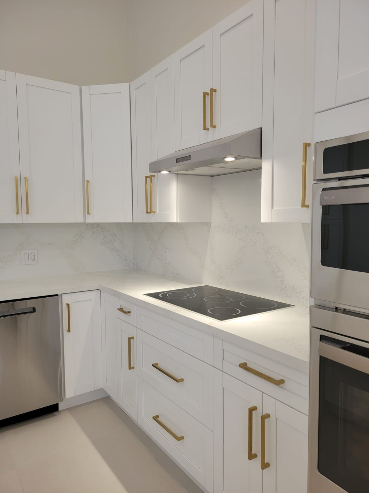 Modern white kitchen with gold hardware, built-in oven, and dark cooktop under a range hood
