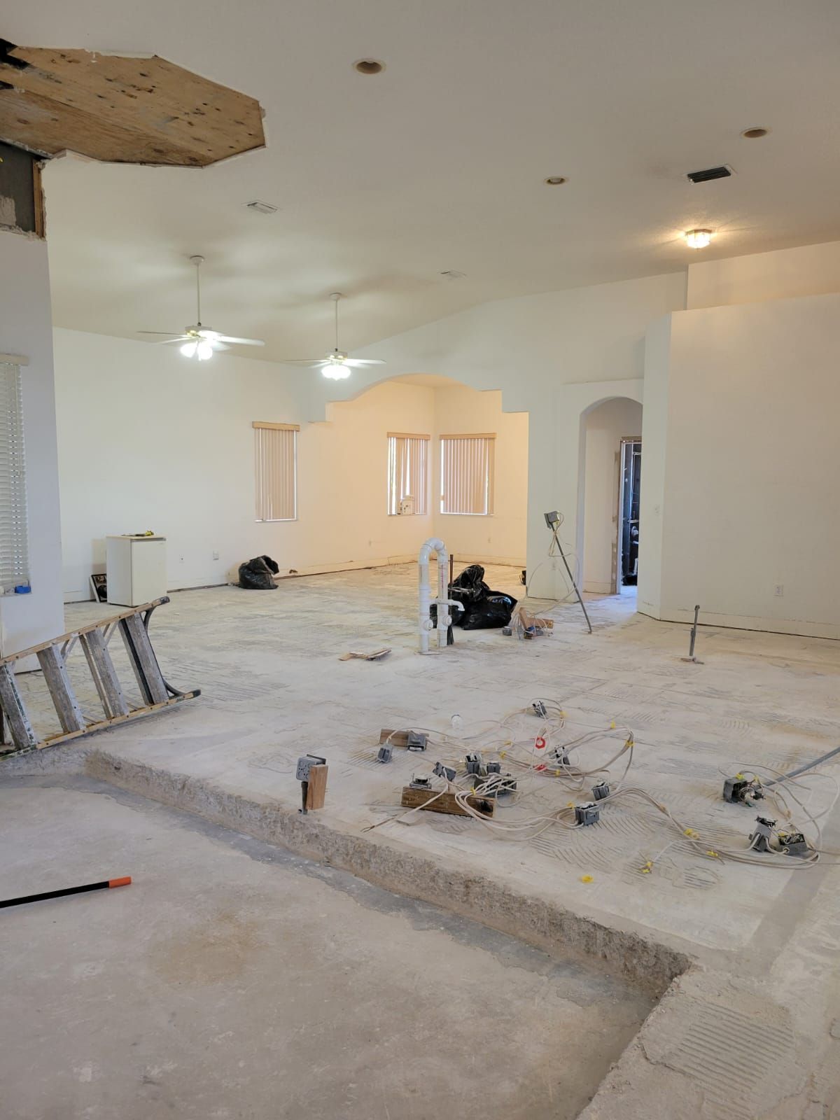 Renovation in progress in a large room with exposed floor, tools, debris, and ladders.