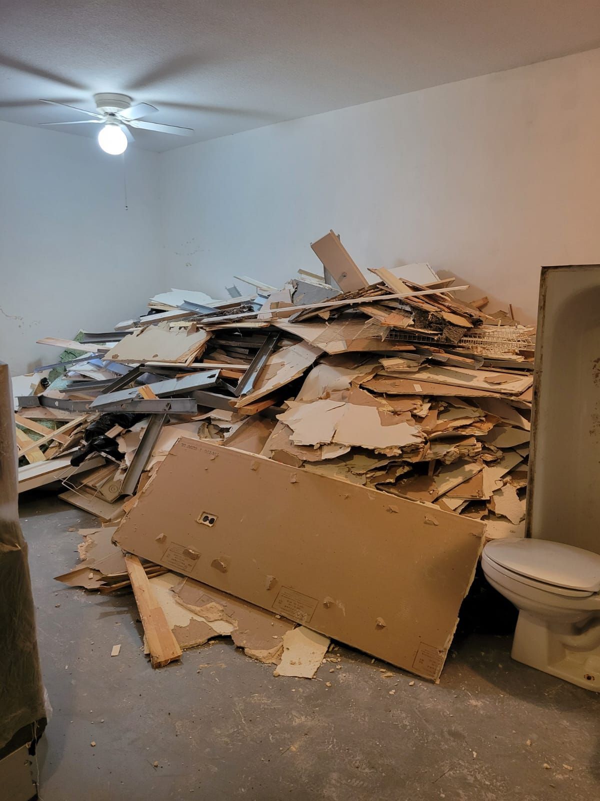 Room cluttered with a large pile of broken cardboard and debris beside a toilet in a bare white room