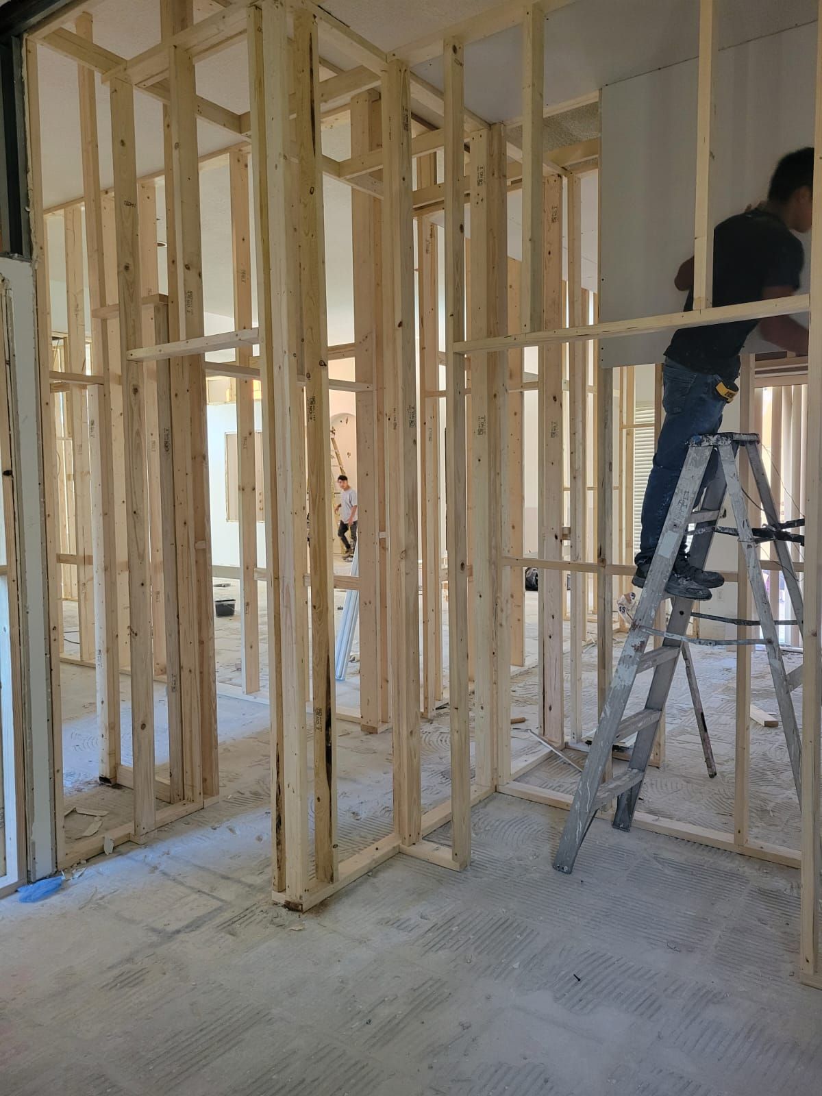 Framing of an unfinished interior with exposed wooden studs and a worker on a ladder.