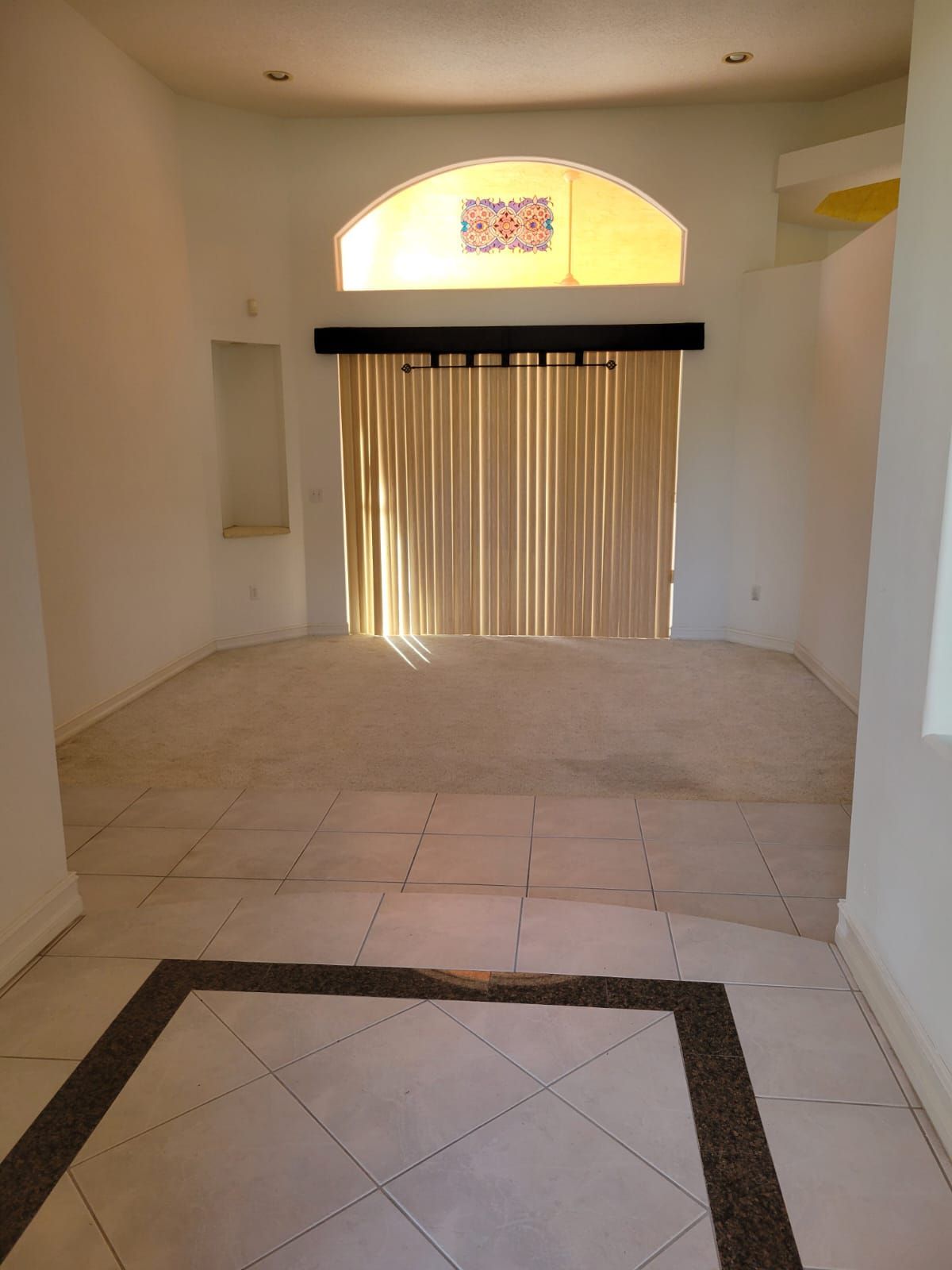 Empty tiled room with arched window and closed vertical blinds, lit by sunlight