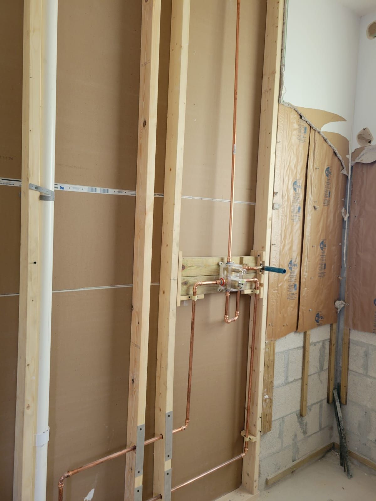 Partially gutted wall with exposed wooden studs, wiring, and plumbing during renovation