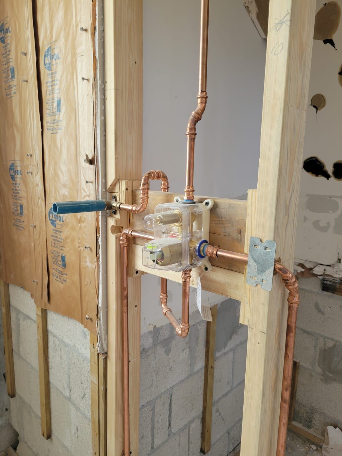Copper plumbing manifold installed in an unfinished wall framed by wood and cinder blocks.