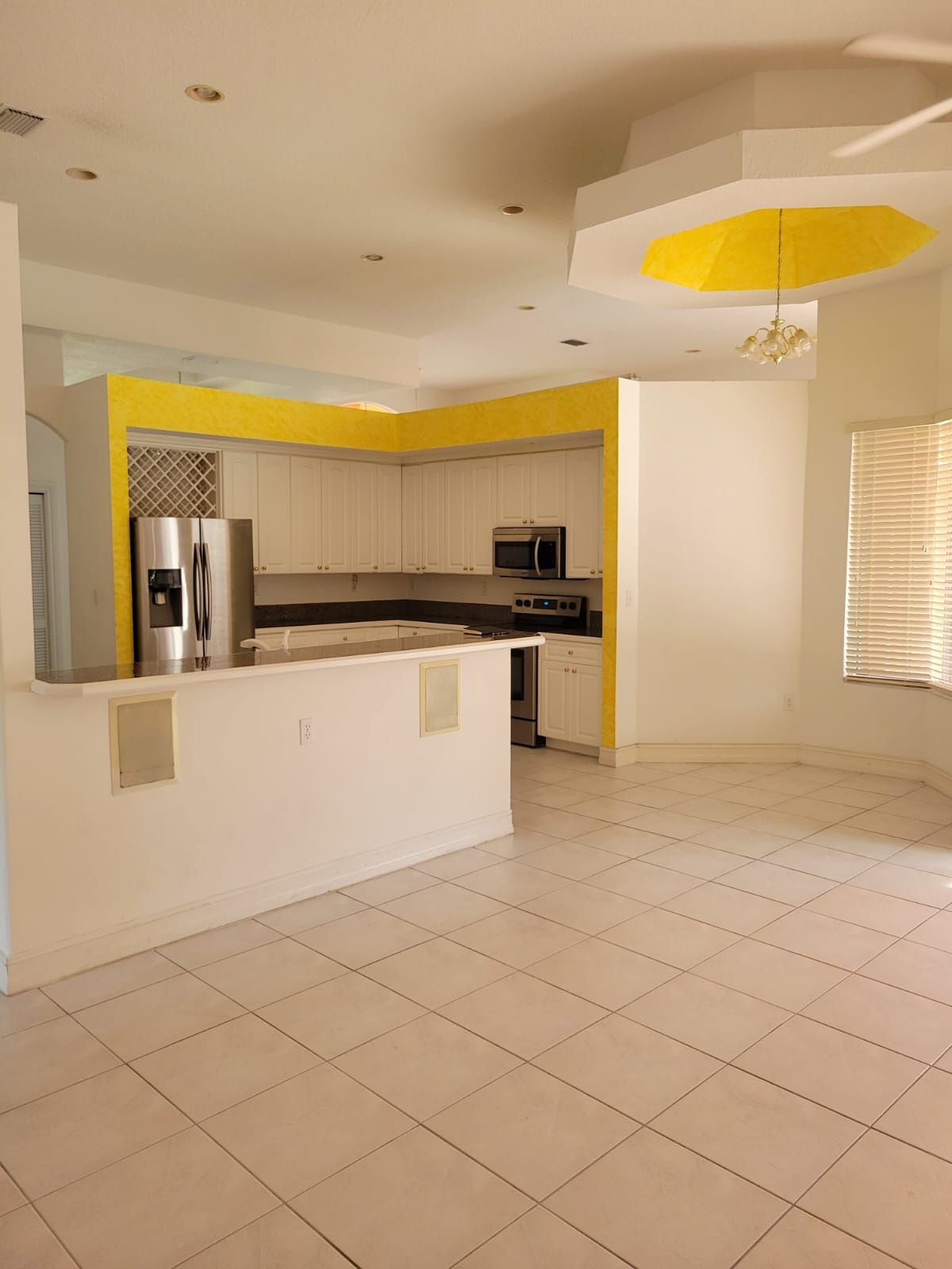 Bright empty kitchen with white cabinets, stainless fridge, yellow accents, and tiled floor