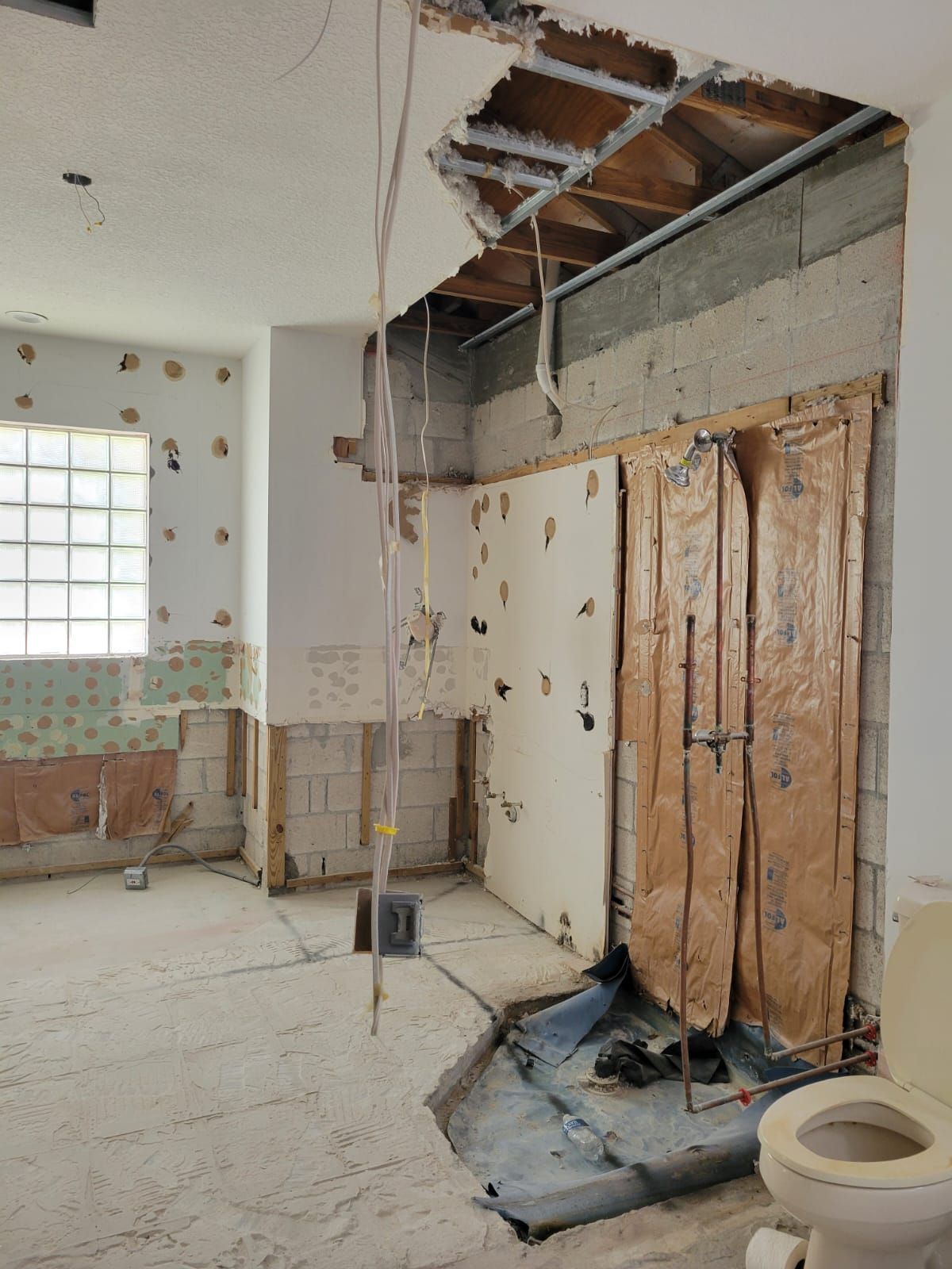 Damaged bathroom with exposed ceiling beams, broken walls, and a wooden cabinet amid renovation debris