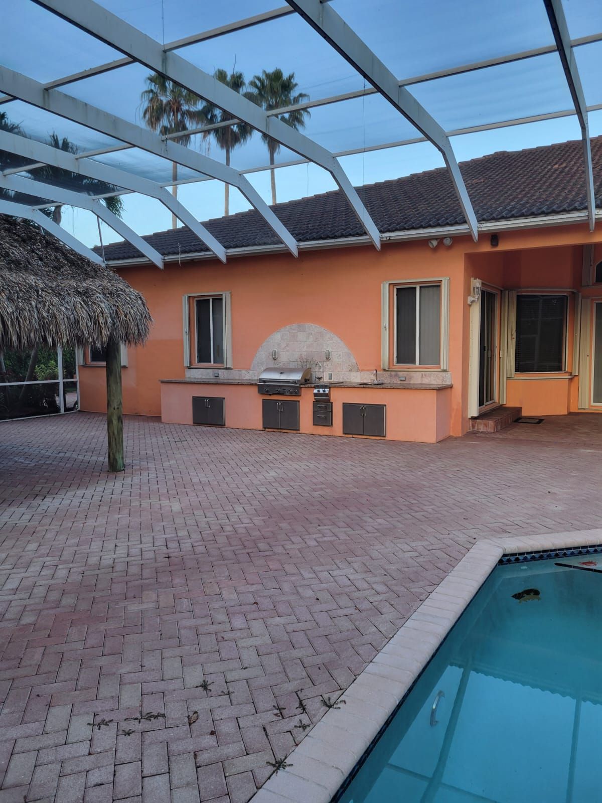Orange patio with brick pavers, covered pergola, grill, and swimming pool corner under blue sky