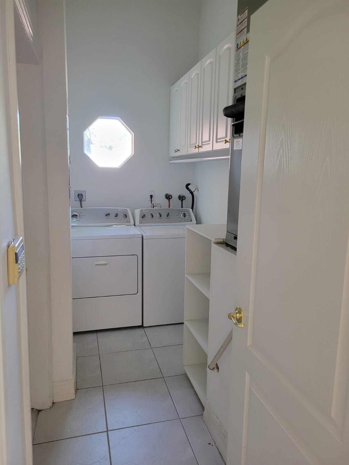 Small white laundry room with washer, sink, wall cabinets, and an octagonal window