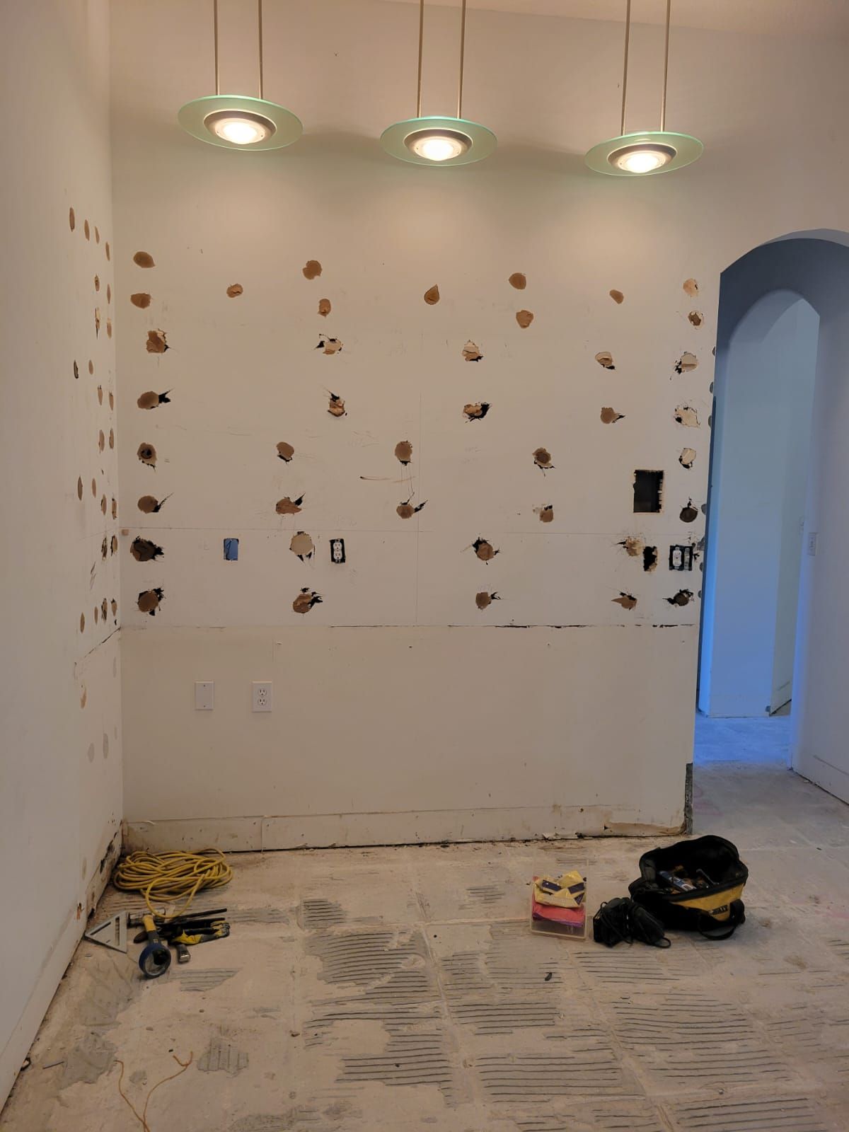 Small room under renovation with wall patches, tools on the floor, and three ceiling lights on.