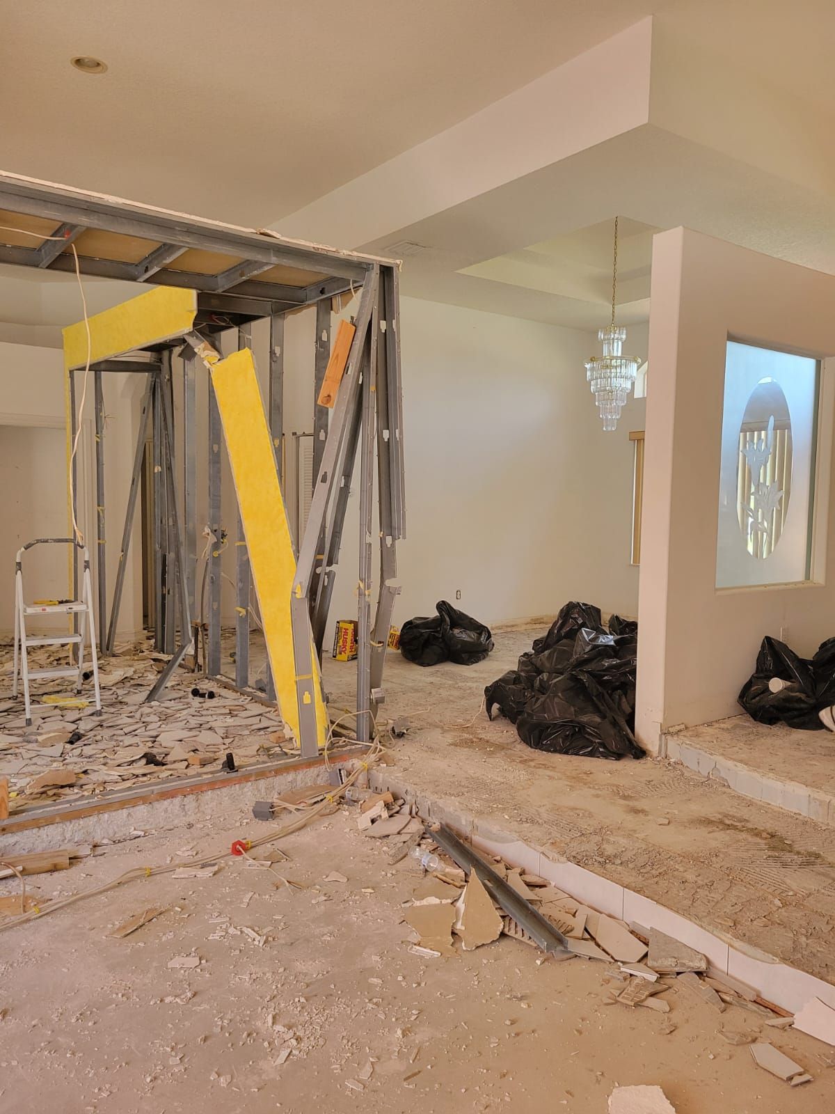 Interior room under renovation with exposed framing, scattered debris, and black trash bags on the floor.