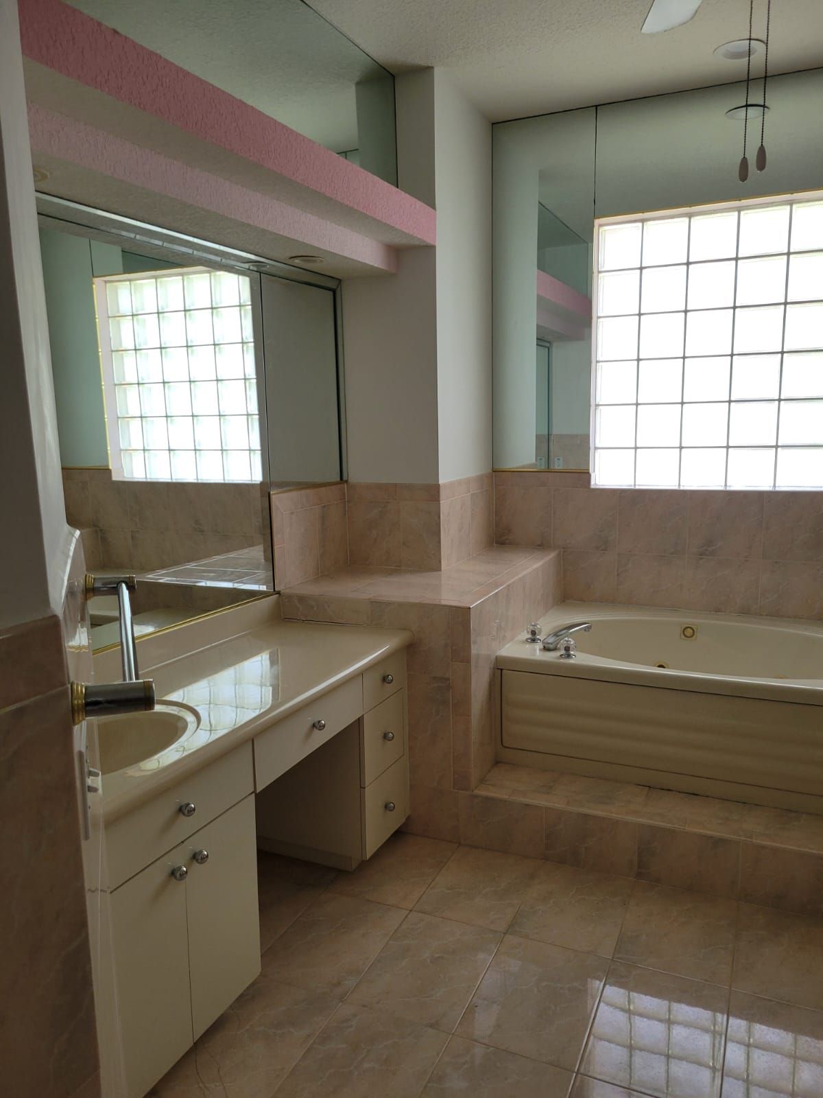 Empty bathroom with sink, bathtub, and large frosted windows, in beige and pink tiles.