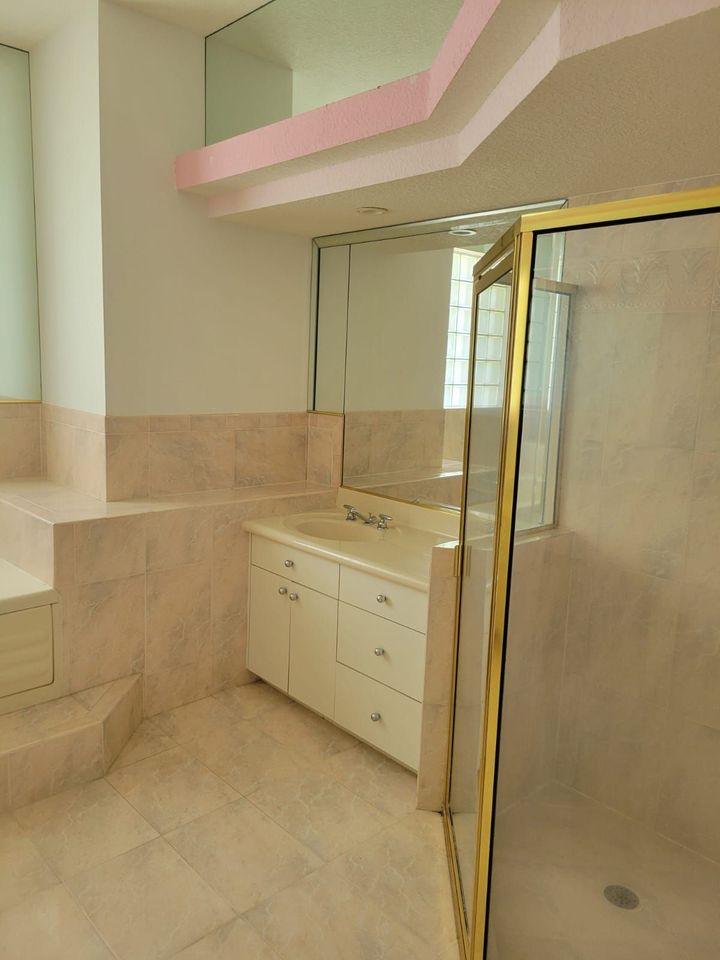 Pink-and-cream bathroom with vanity, mirror, tiled bench, and glass shower door